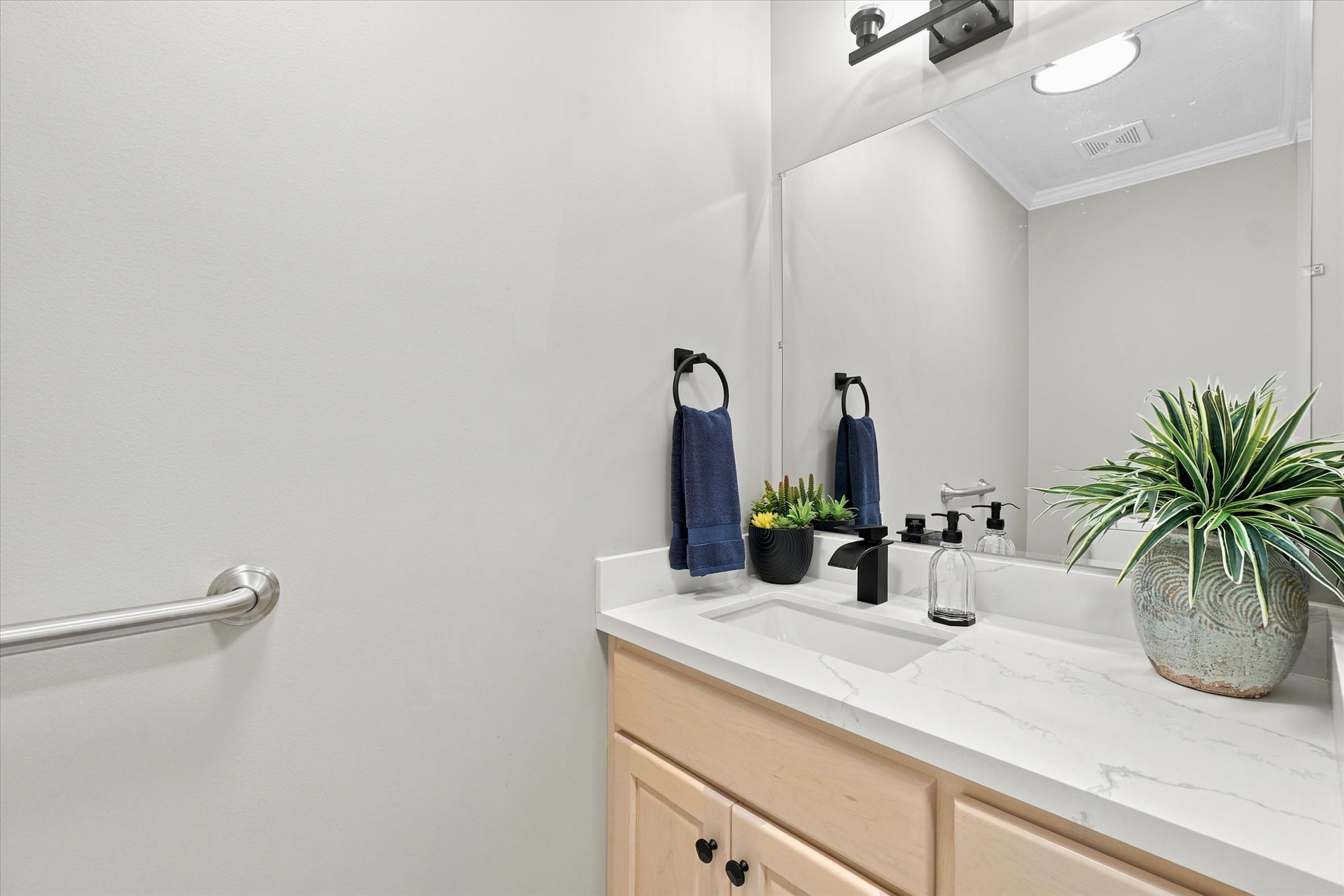 Bathroom vanity featuring a light wood-finish cabinet with black hardware, a white countertop with integrated sink, and a large wall-mounted mirror