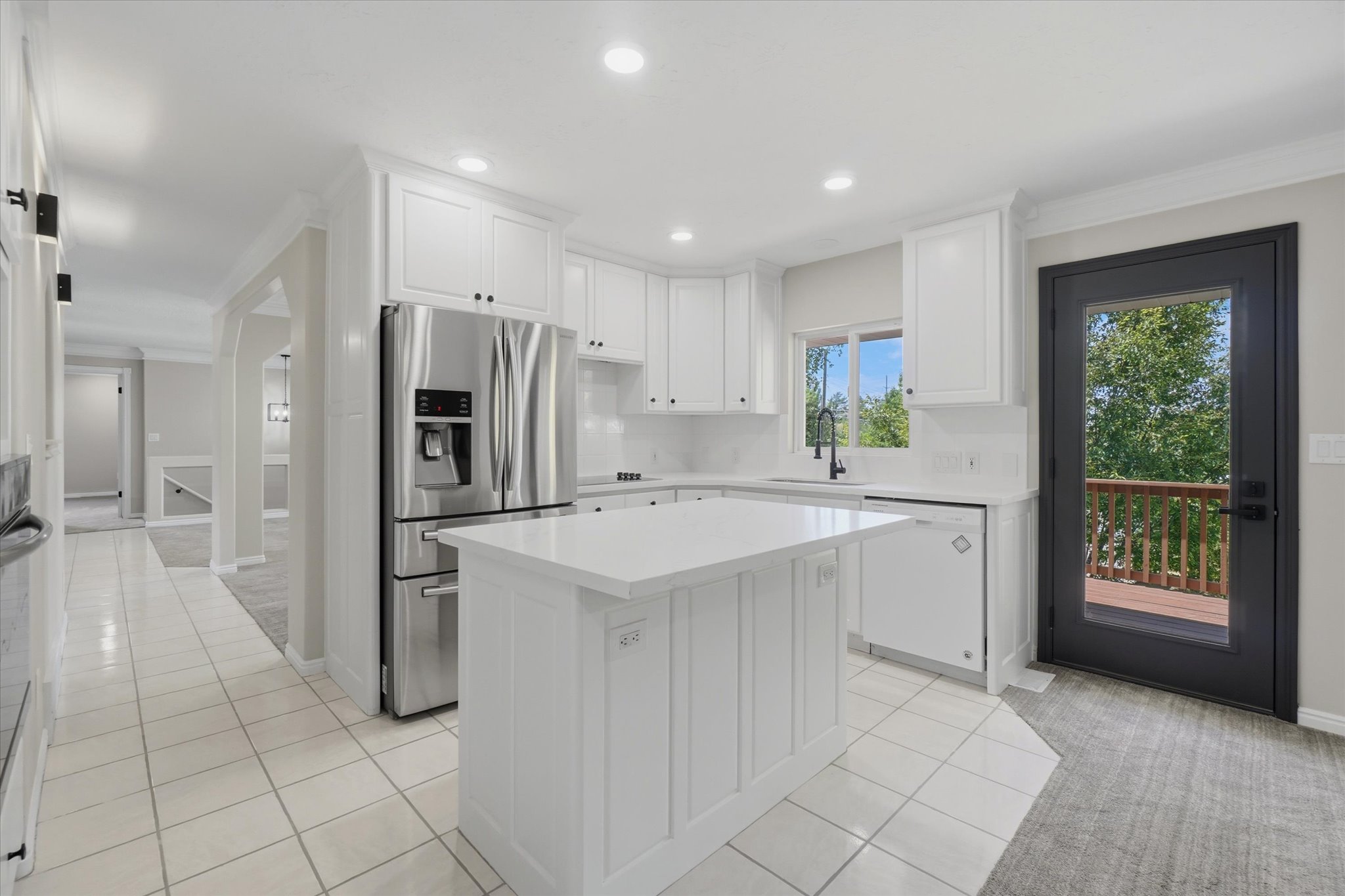 Bright kitchen featuring white cabinetry, a central island with a solid surface quartz countertop, stainless steel refrigerator, and a glass-paneled exterior door opening to a deck
