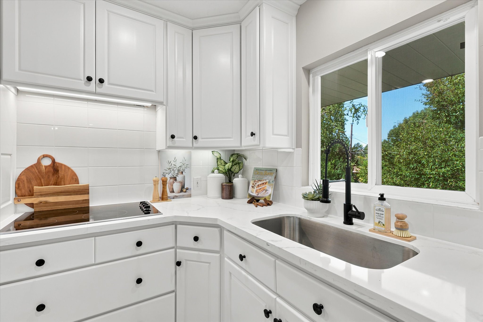 Bright kitchen featuring white shaker cabinetry, white subway tile backsplash, white countertops, stainless steel undermount sink, and a black gooseneck faucet