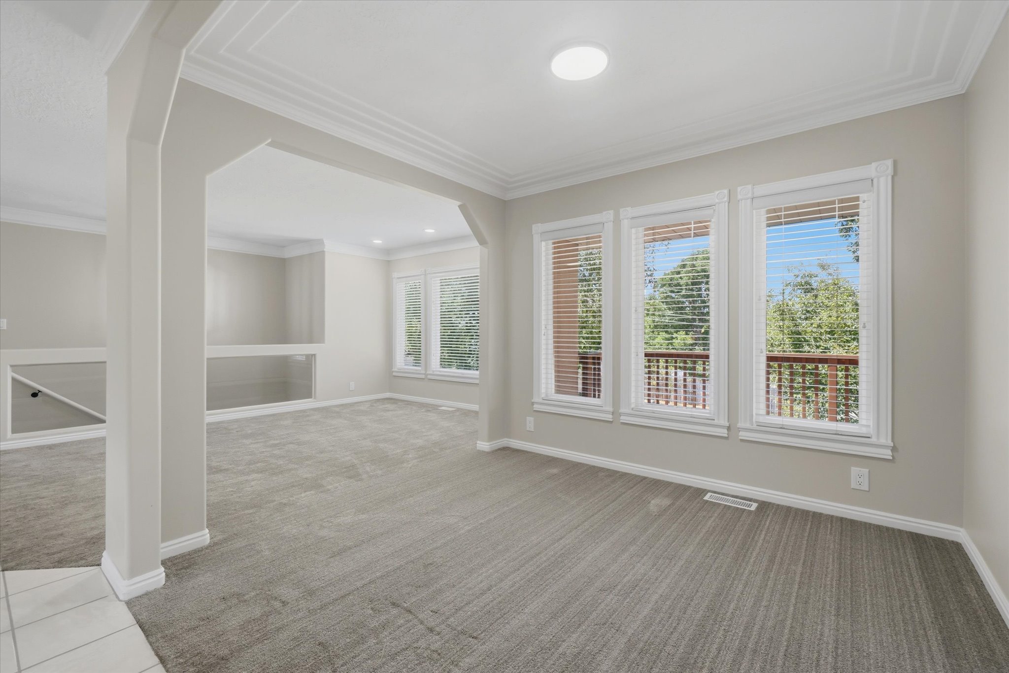 Spacious interior room with light gray carpeting and three large windows, could be used as a formal dining area.