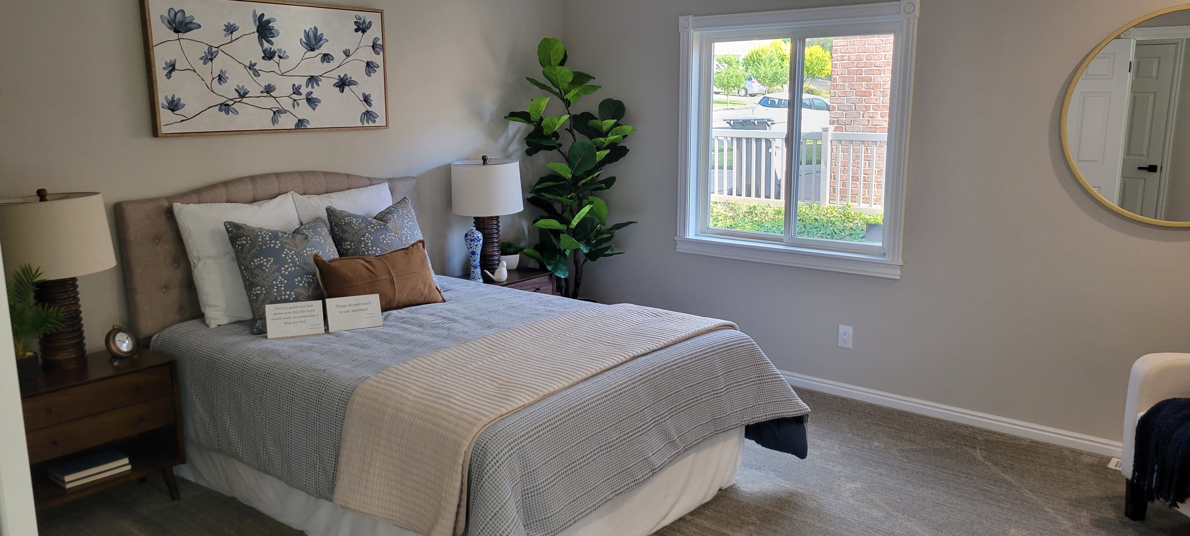 Neutral-toned bedroom featuring a large window, plush carpet, and white baseboards