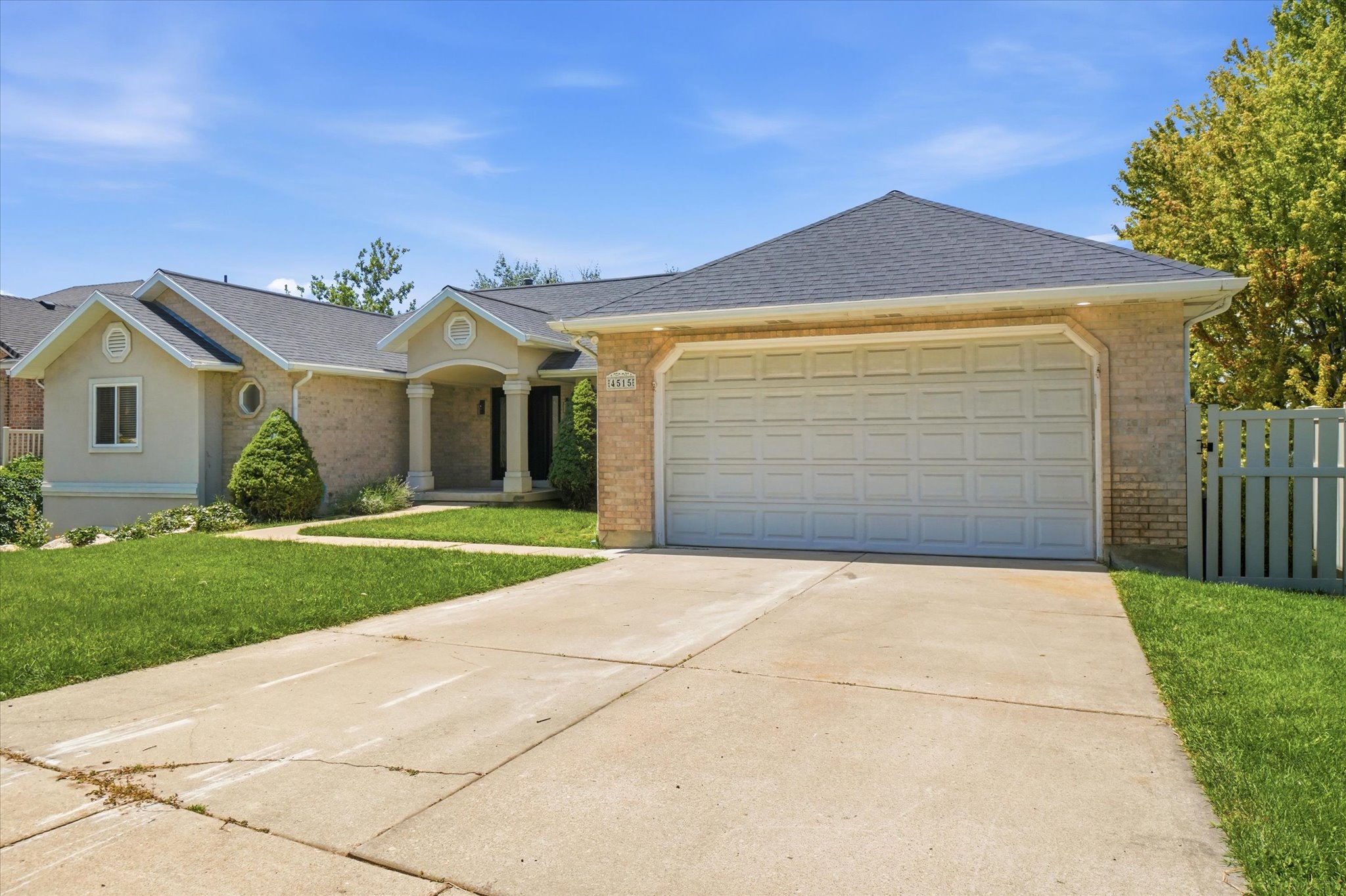 Brick and stucco facade featuring a two-car garage, a covered entry with columns, a dark shingle roof, and a concrete driveway