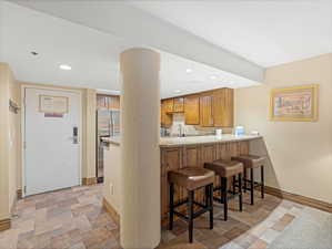Kitchenette featuring wood cabinetry, stainless steel refrigerator, and built-in bar seating with three stools