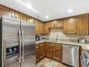 Kitchen featuring wood cabinetry, stainless steel appliances, a double basin sink with a gooseneck faucet, light-toned countertops, and mosaic-style floor tiles