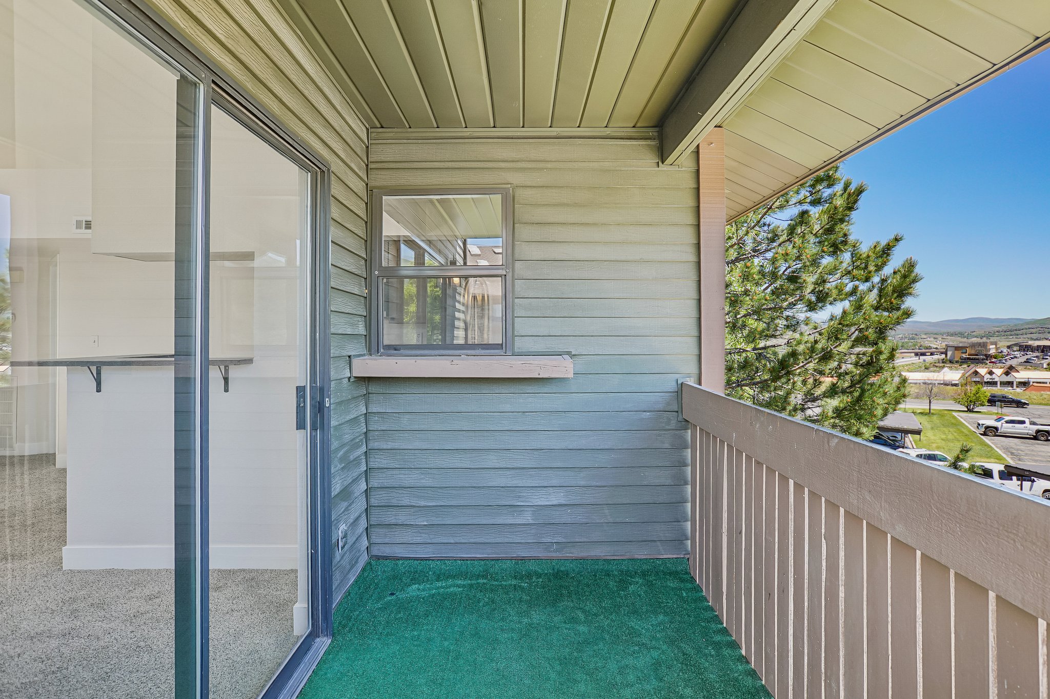 Balcony with green artificial turf flooring, featuring horizontal siding, a framed window, and a light-colored railing