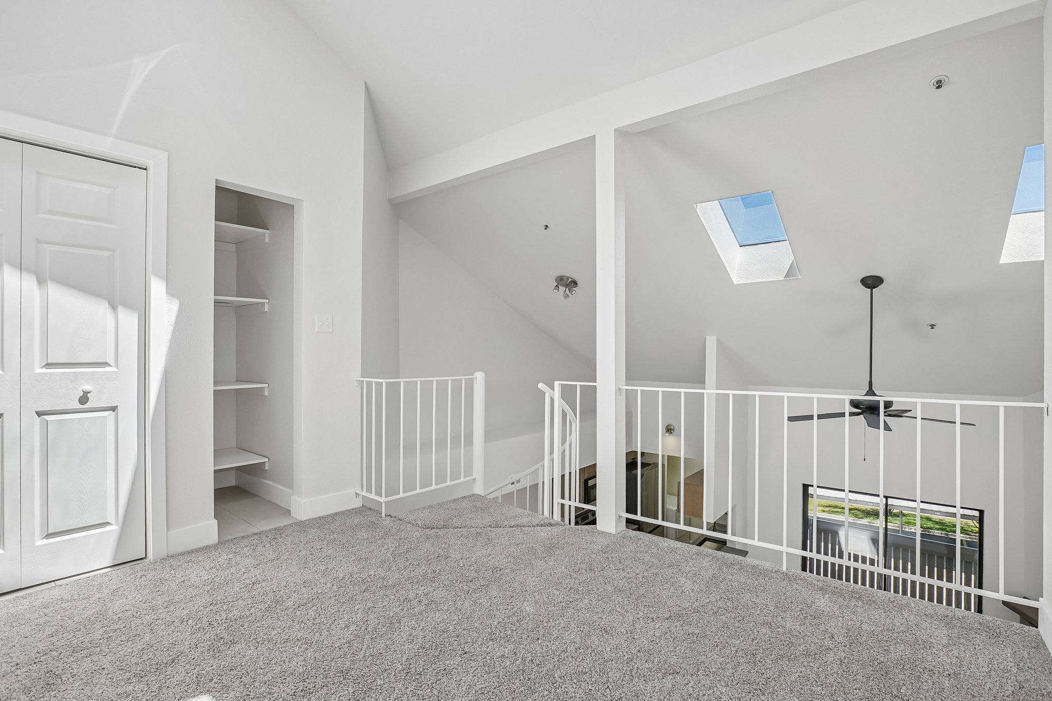 Loft area featuring vaulted ceilings, two skylights, a ceiling fan, and white railing overlooking the lower level