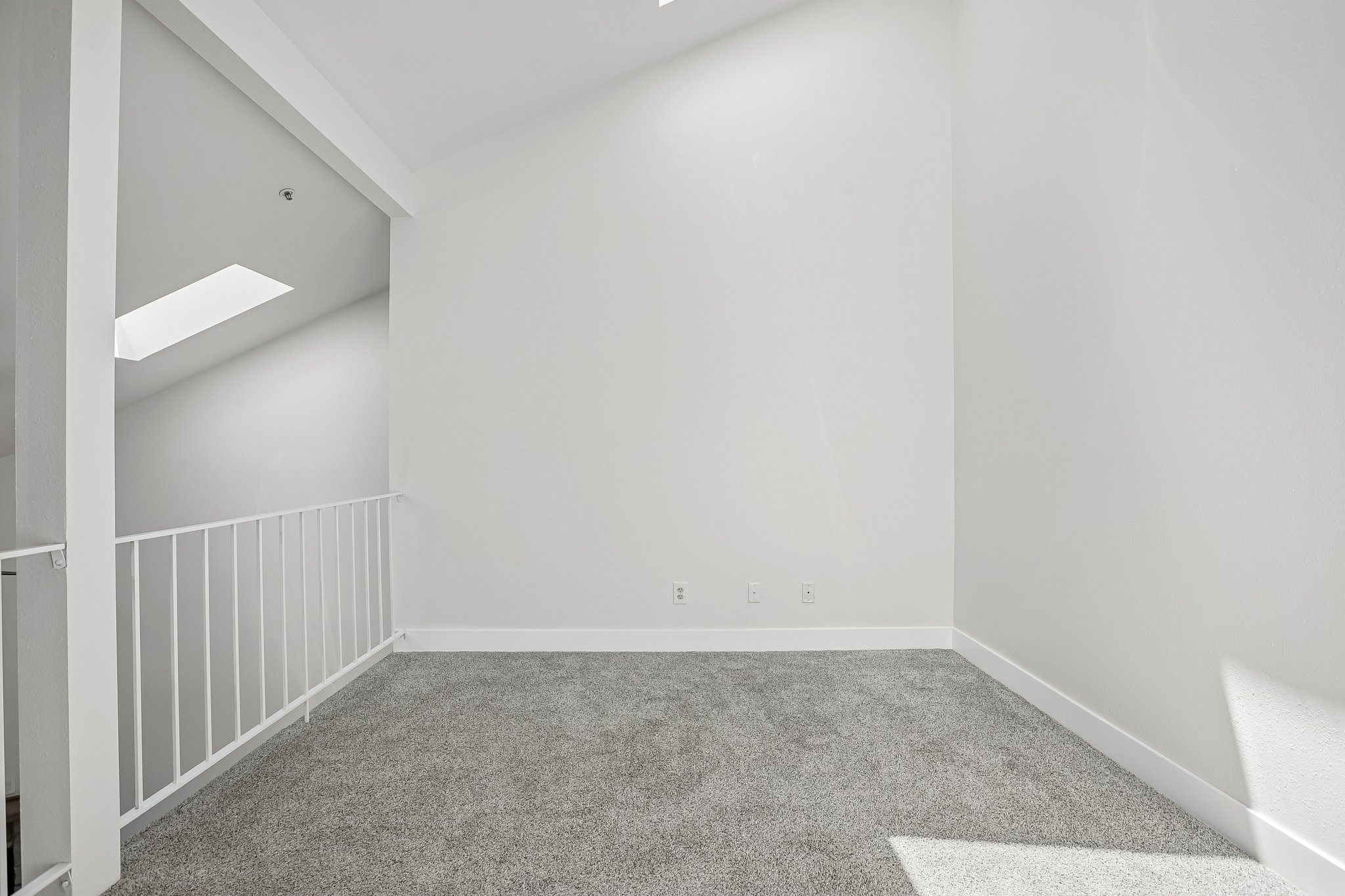 Carpeted loft area featuring a white railing, vaulted ceiling, and a skylight