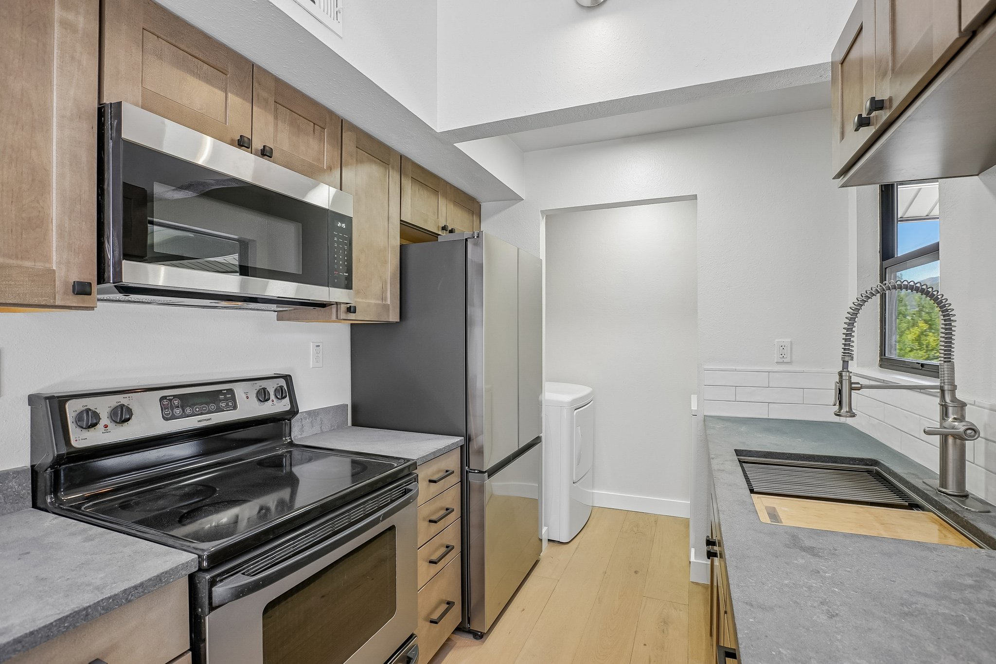 Galley kitchen featuring stainless steel appliances, light wood-finish cabinetry, and dark countertops