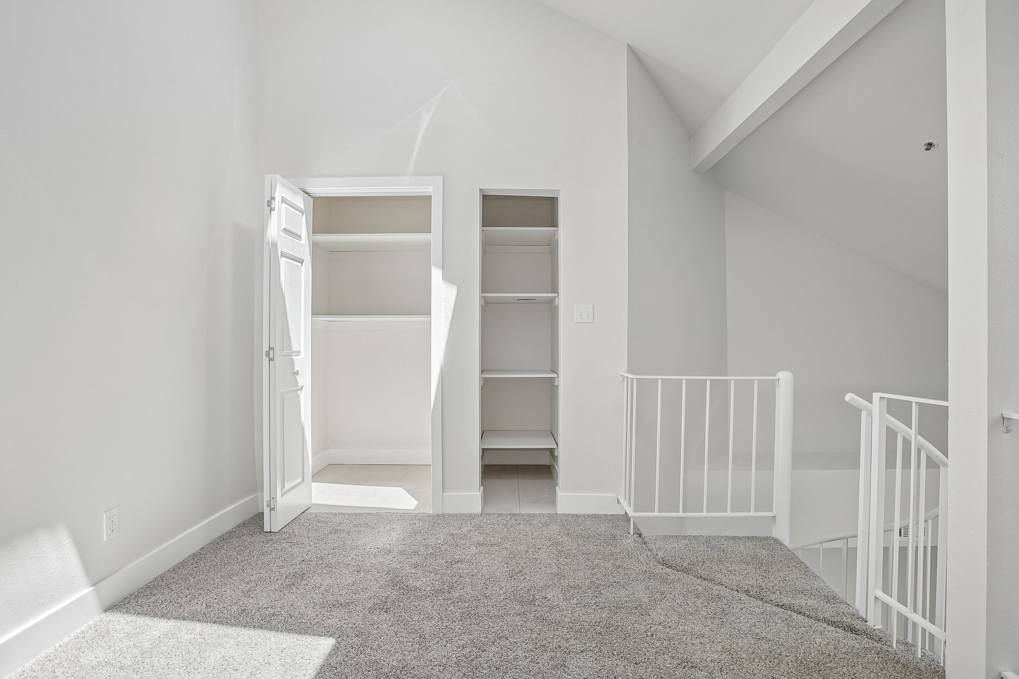 Carpeted loft area featuring a white metal railing, built-in shelving, a recessed closet with an open door, vaulted ceilings, and white painted walls