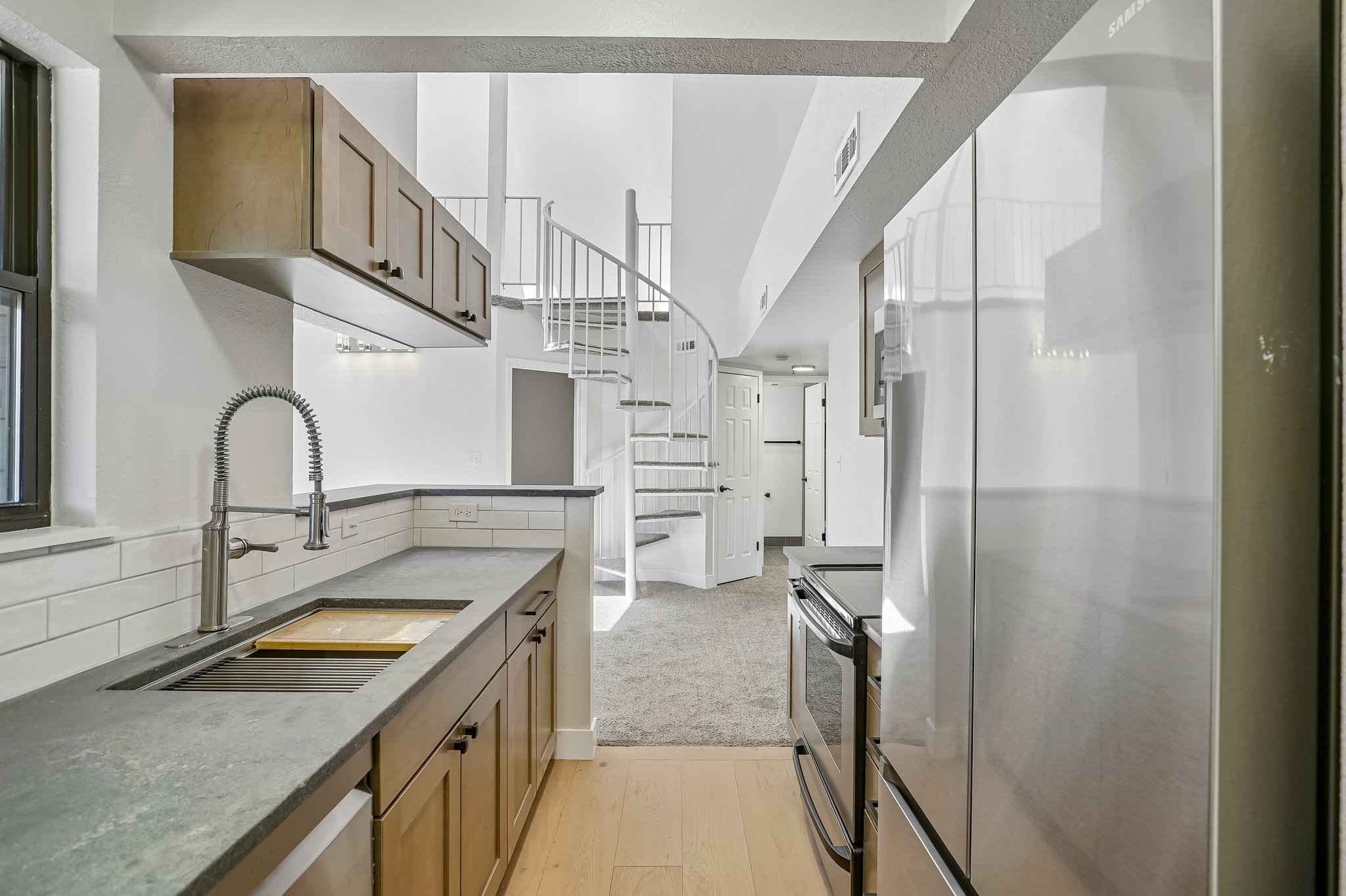 Modern kitchen featuring a stainless steel sink with a high-arc faucet, solid surface countertops, and wood cabinetry