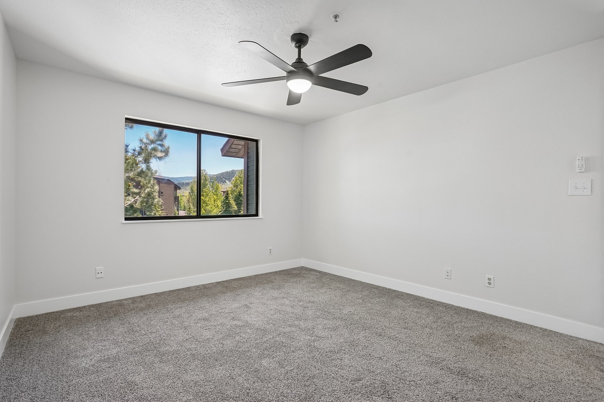 Carpeted room featuring a large window with mountain scenery, a ceiling fan with integrated lighting, and white baseboards