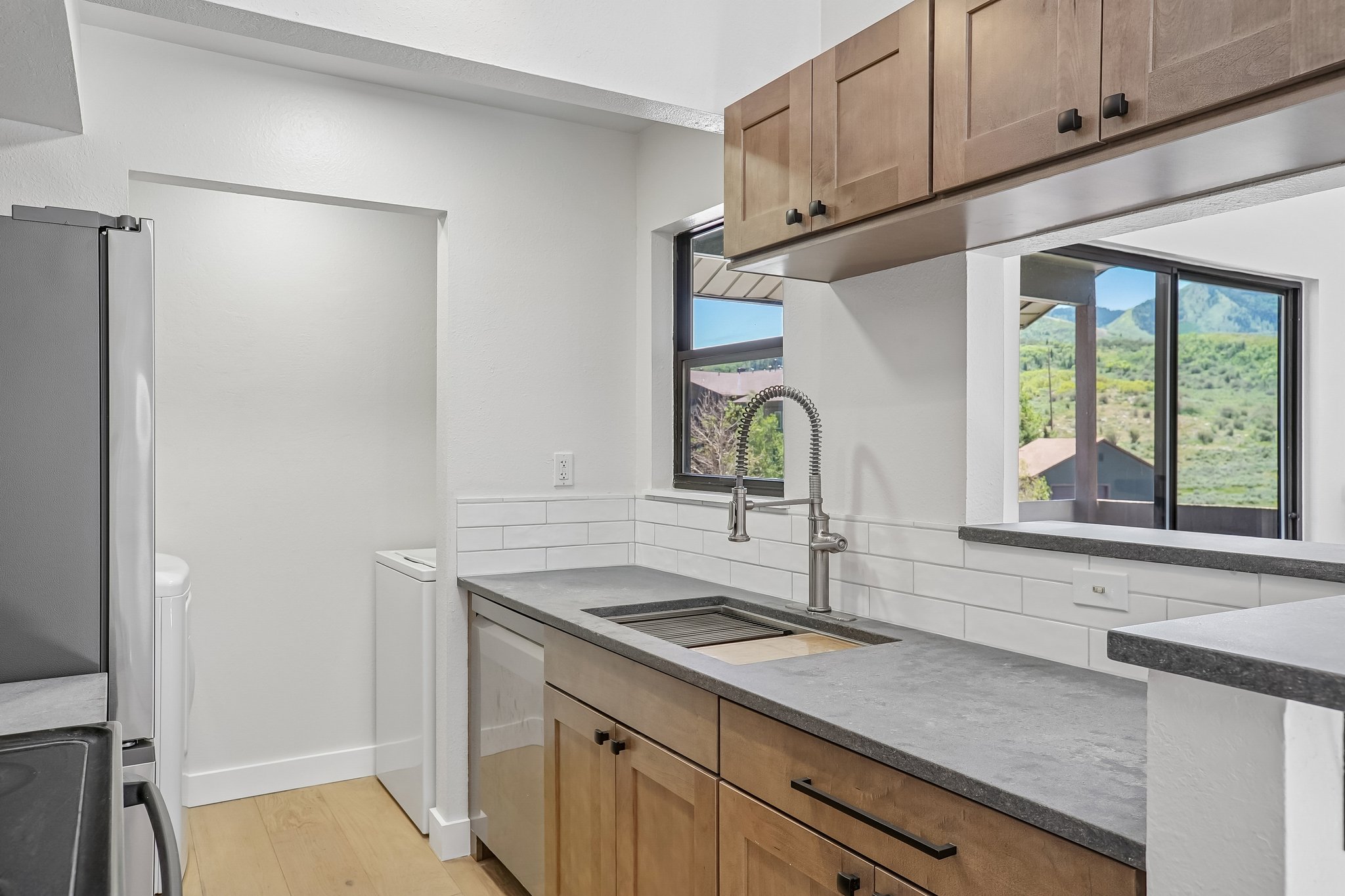 Modern kitchen featuring wood-finish cabinetry, solid surface countertops, a subway tile backsplash, and a stainless steel gooseneck faucet
