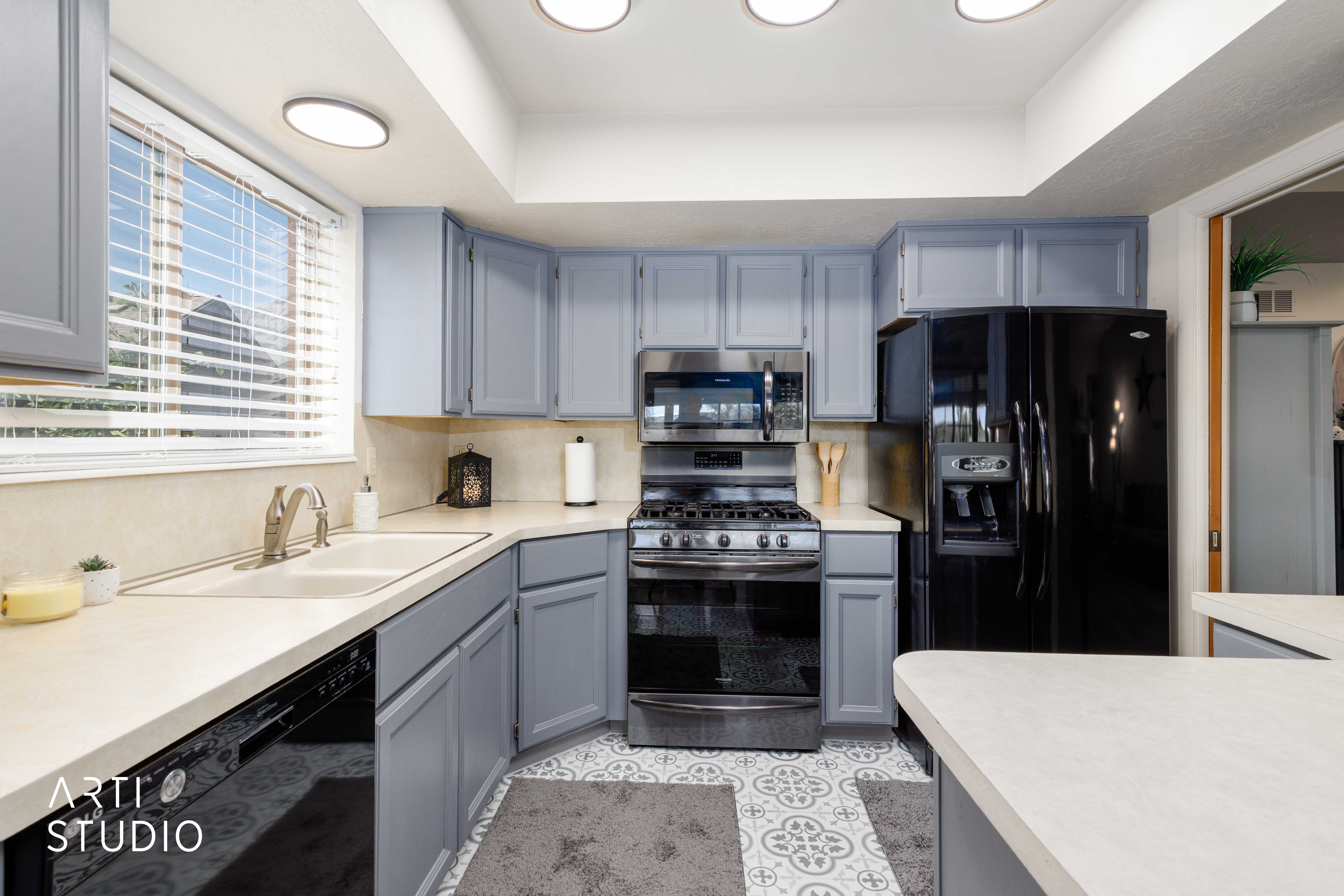 Kitchen featuring gray cabinetry, light countertops, an integrated sink, a stainless steel range with microwave, and patterned floor tile
