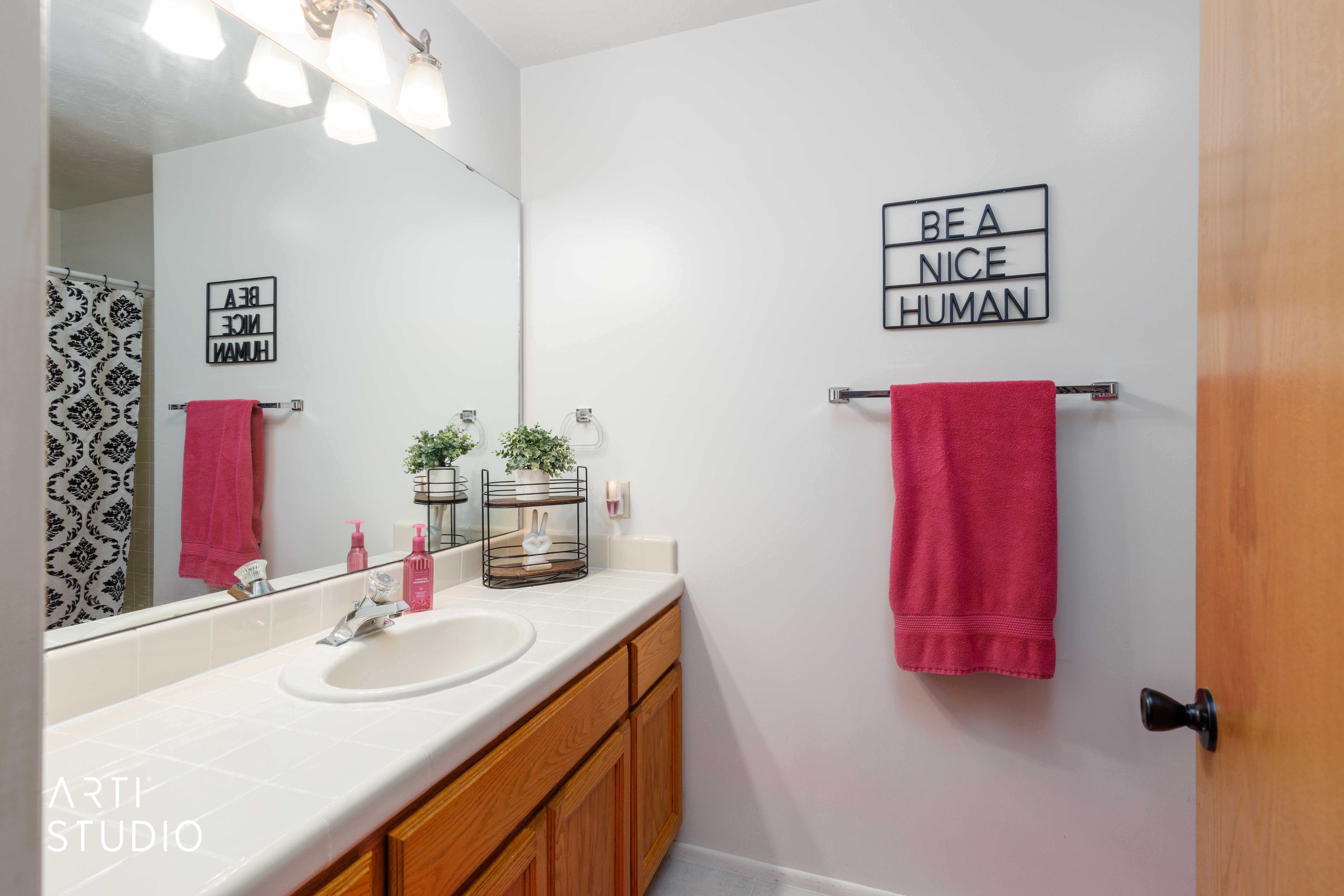 Bathroom vanity featuring a light-toned countertop with integrated sink, wood-finish cabinetry, and an expansive mirror