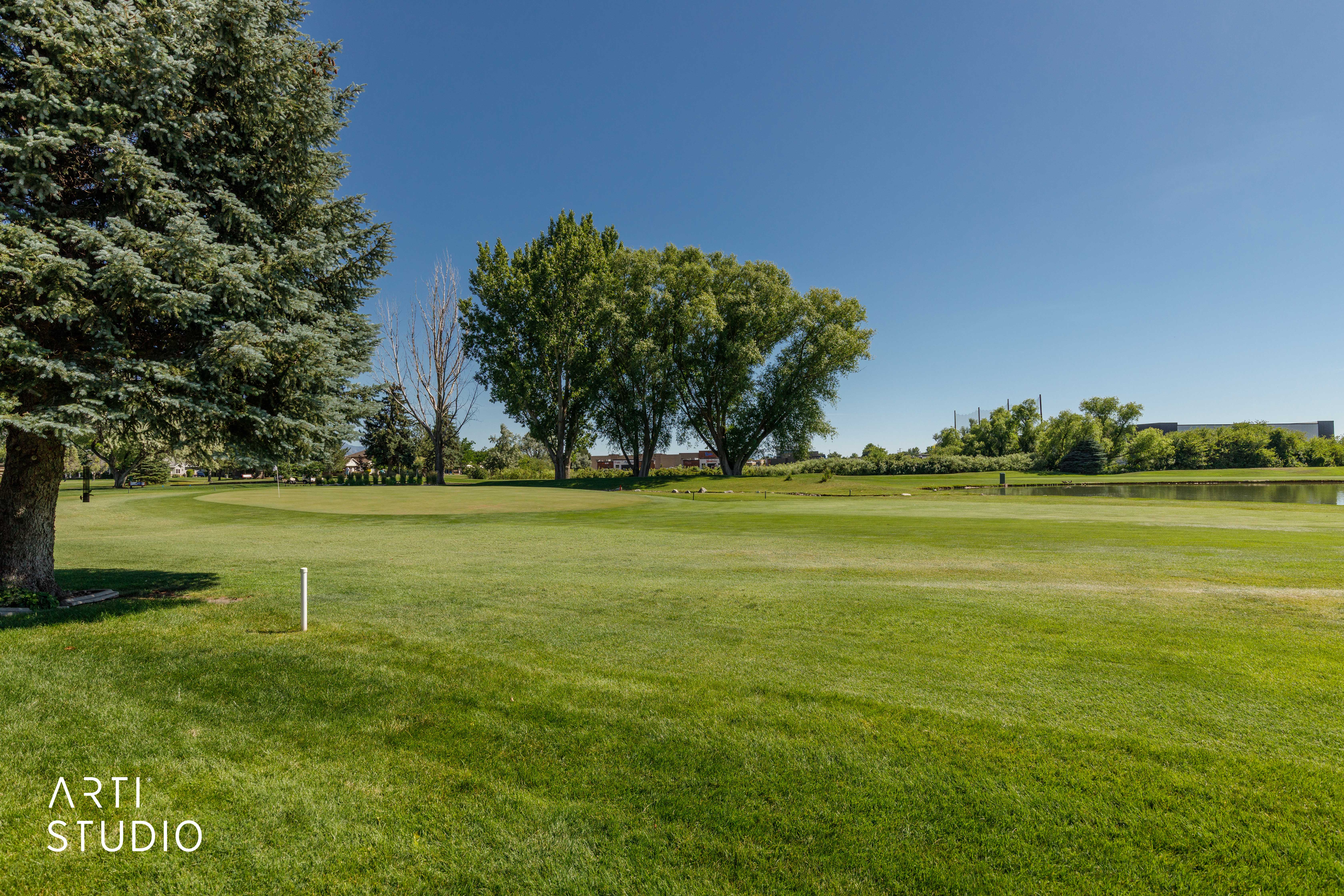 Expansive golf course green with a manicured lawn, established trees, and a distant water feature