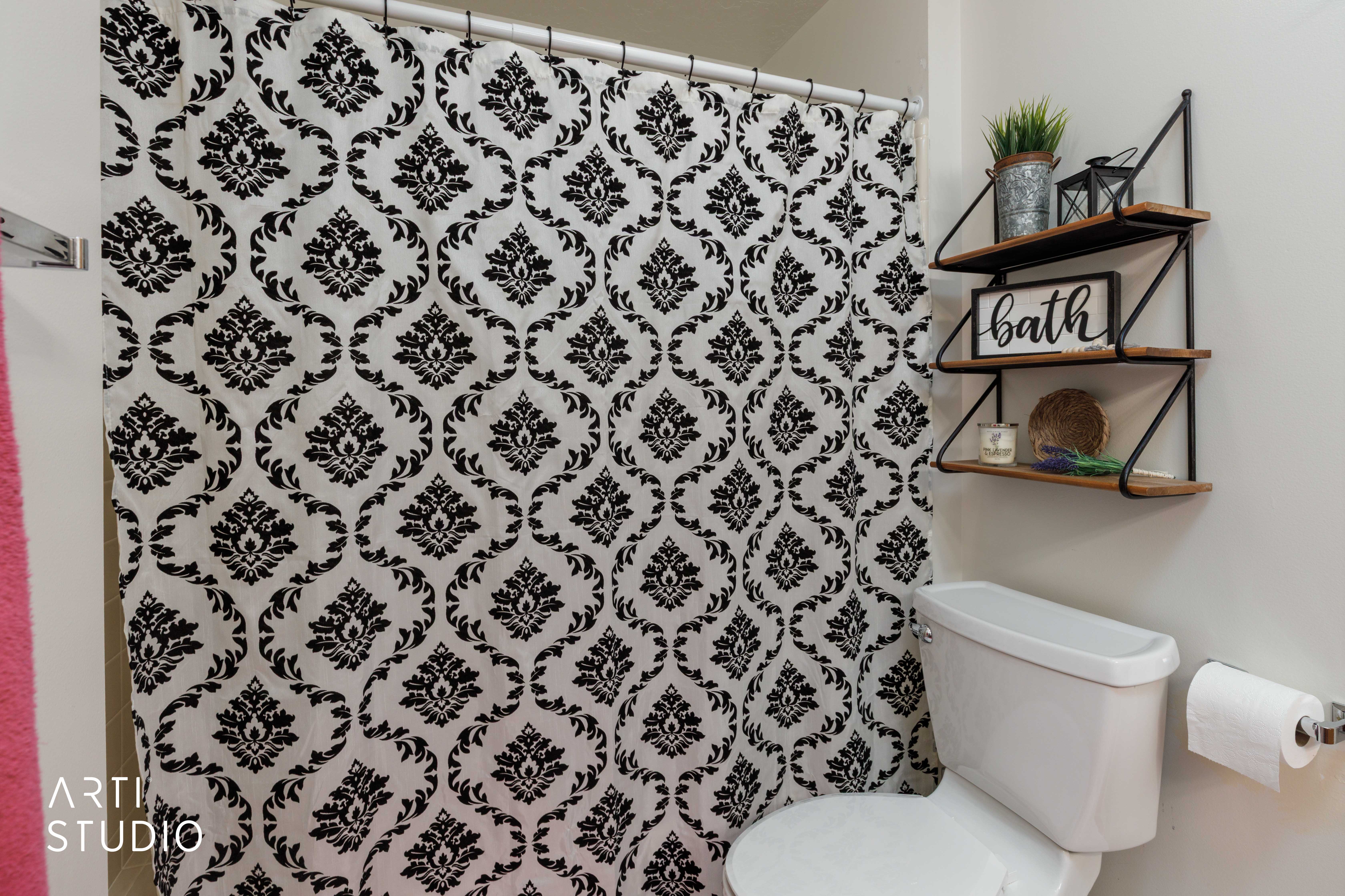 White toilet with a wall-mounted paper holder and a three-tier shelving unit featuring wood-finish shelves and black metal brackets