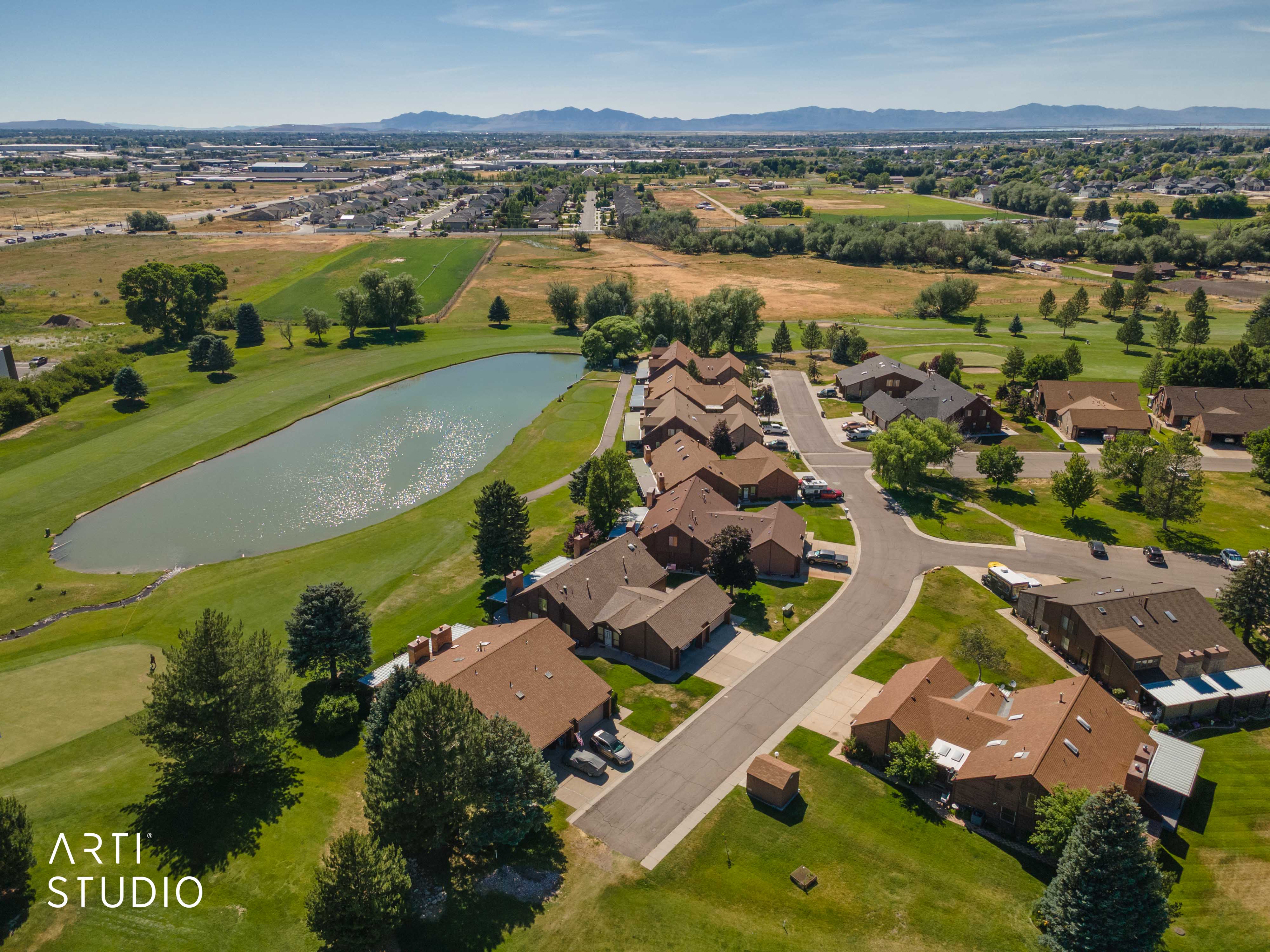 Aerial perspective showcasing a residential community situated alongside a golf course with an elongated pond
