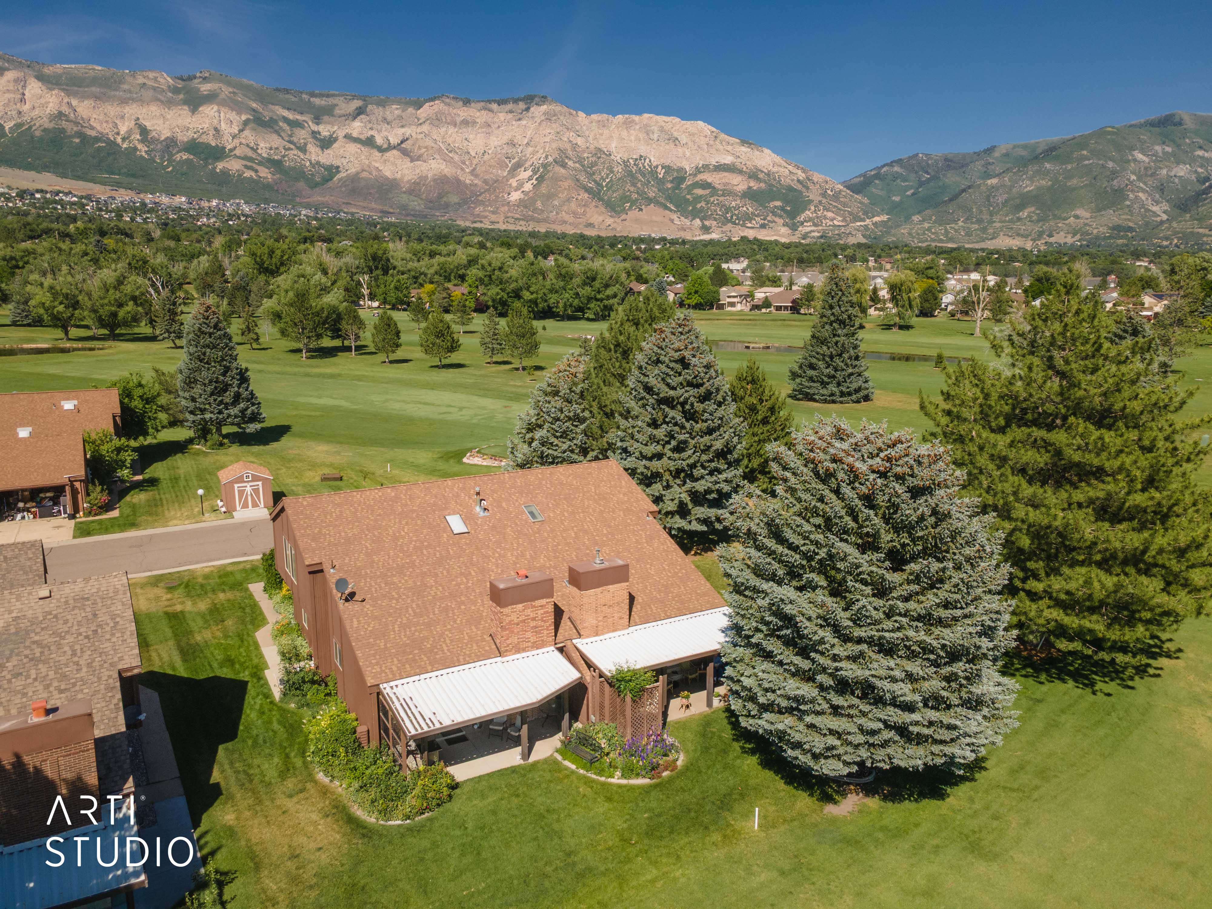 Property featuring a brown shingle roof and covered patio, bordered by mature evergreen trees