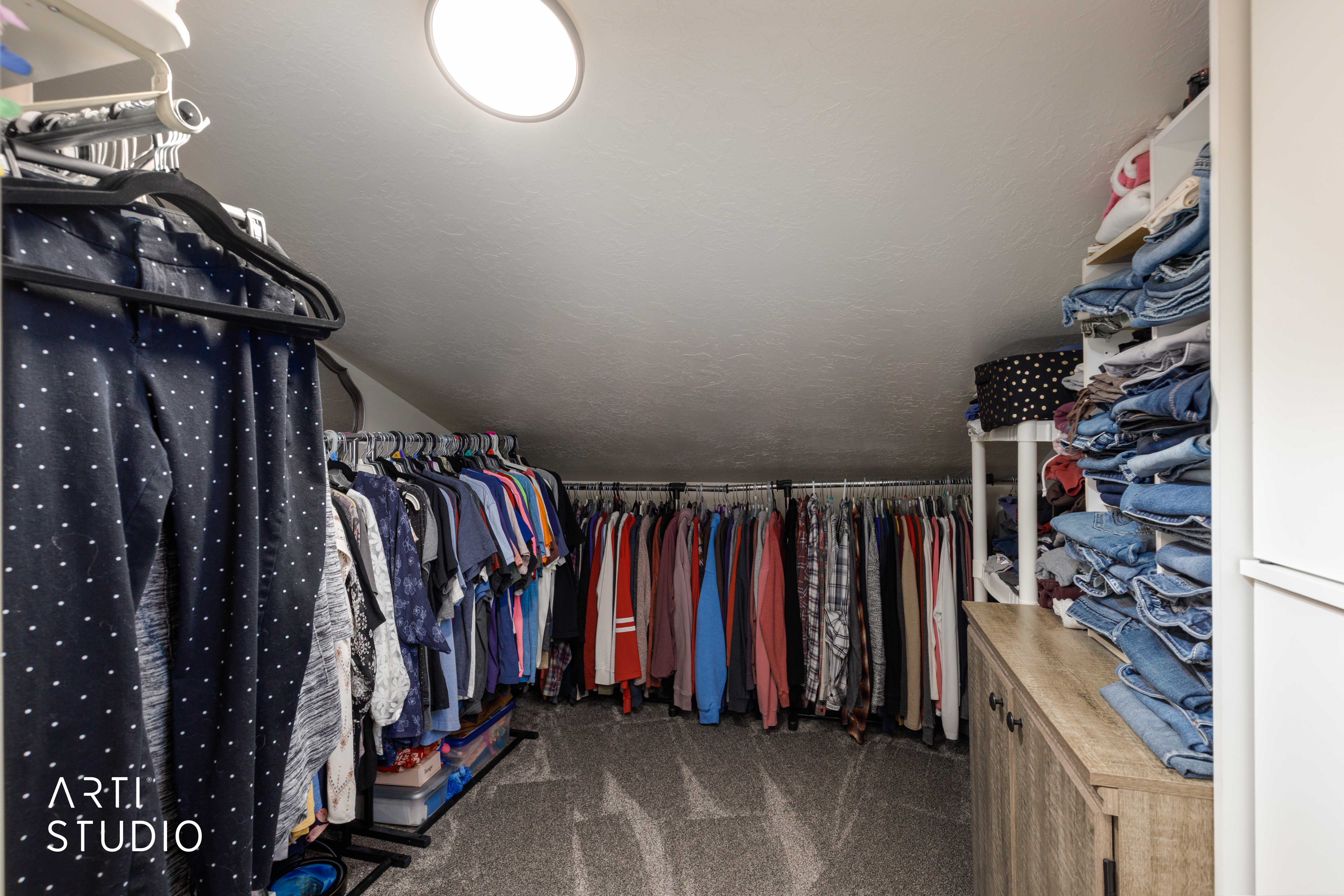 Walk-in closet featuring sloped ceilings, recessed lighting, wall-mounted hanging rods, and built-in shelving with wood-finish cabinetry