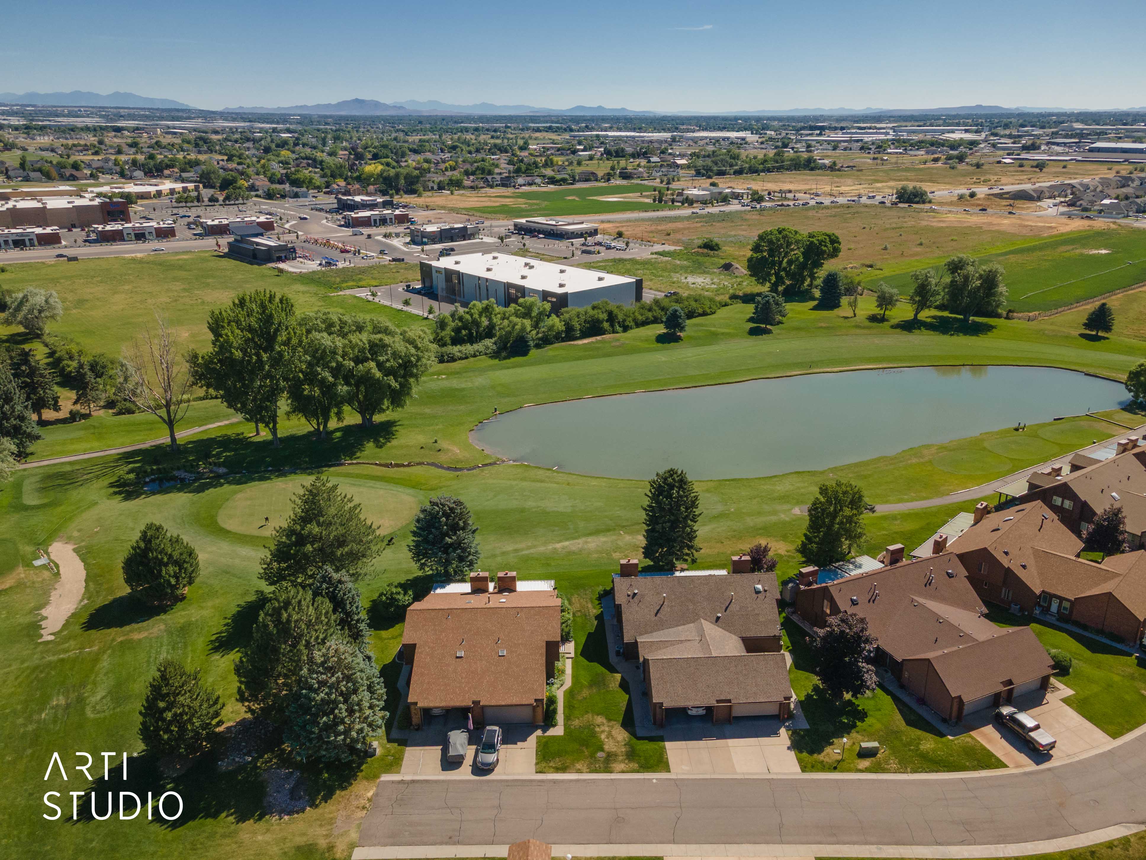 Residential properties bordering a golf course with a prominent pond feature and distant mountains