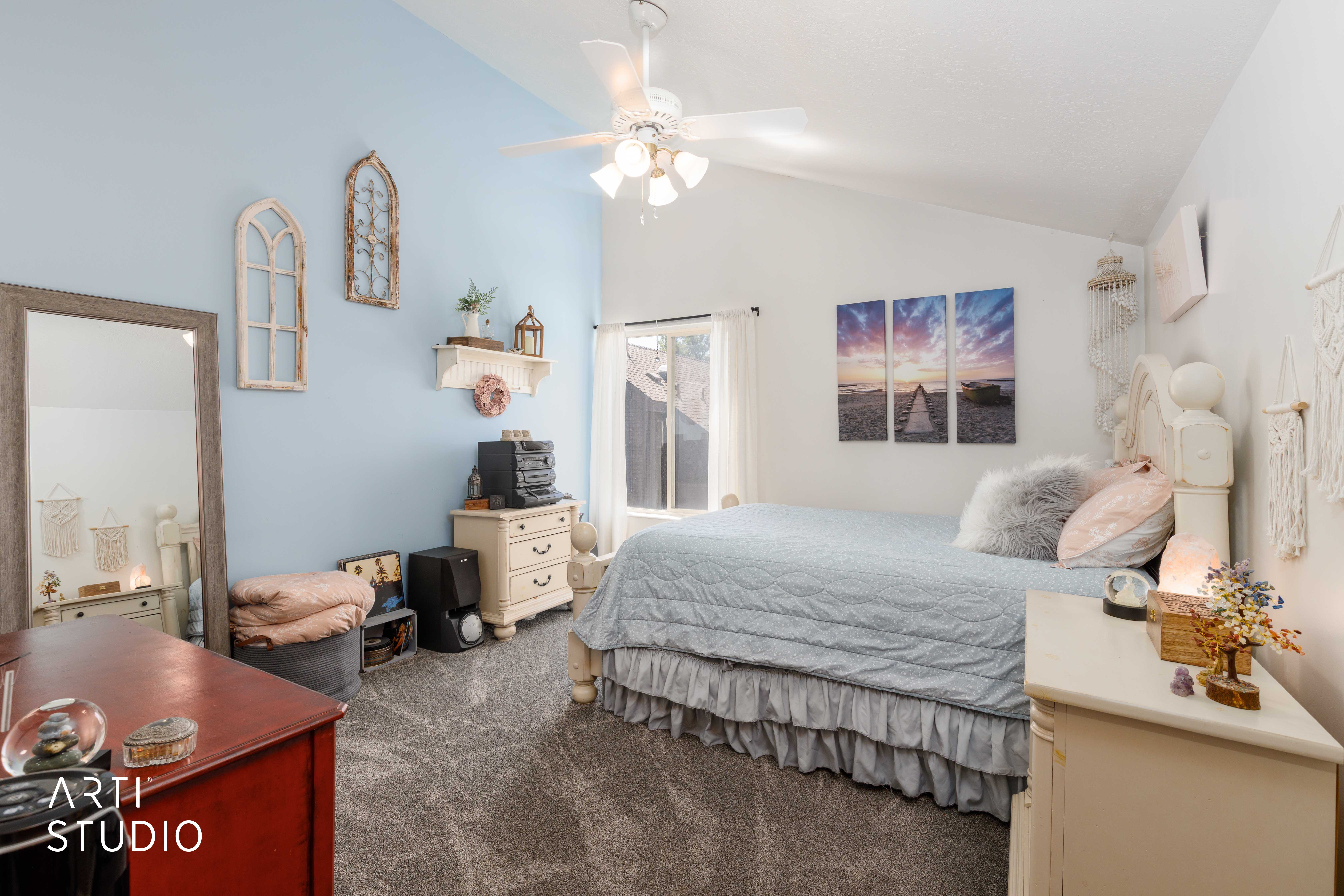 Vaulted ceiling bedroom featuring light blue and white walls, grey carpet, a ceiling fan, and a window with white drapes
