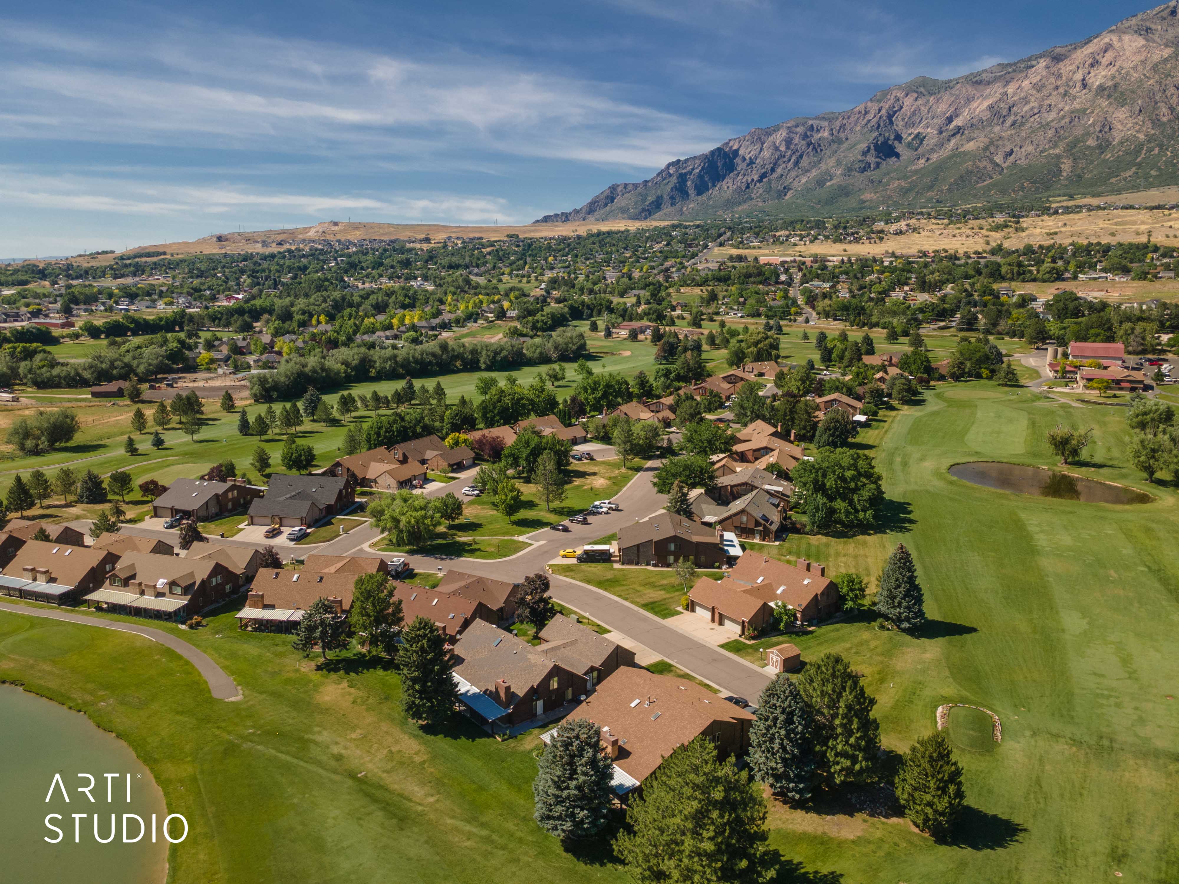 Aerial perspective showcasing residential properties bordering a golf course with mountainous terrain in the background