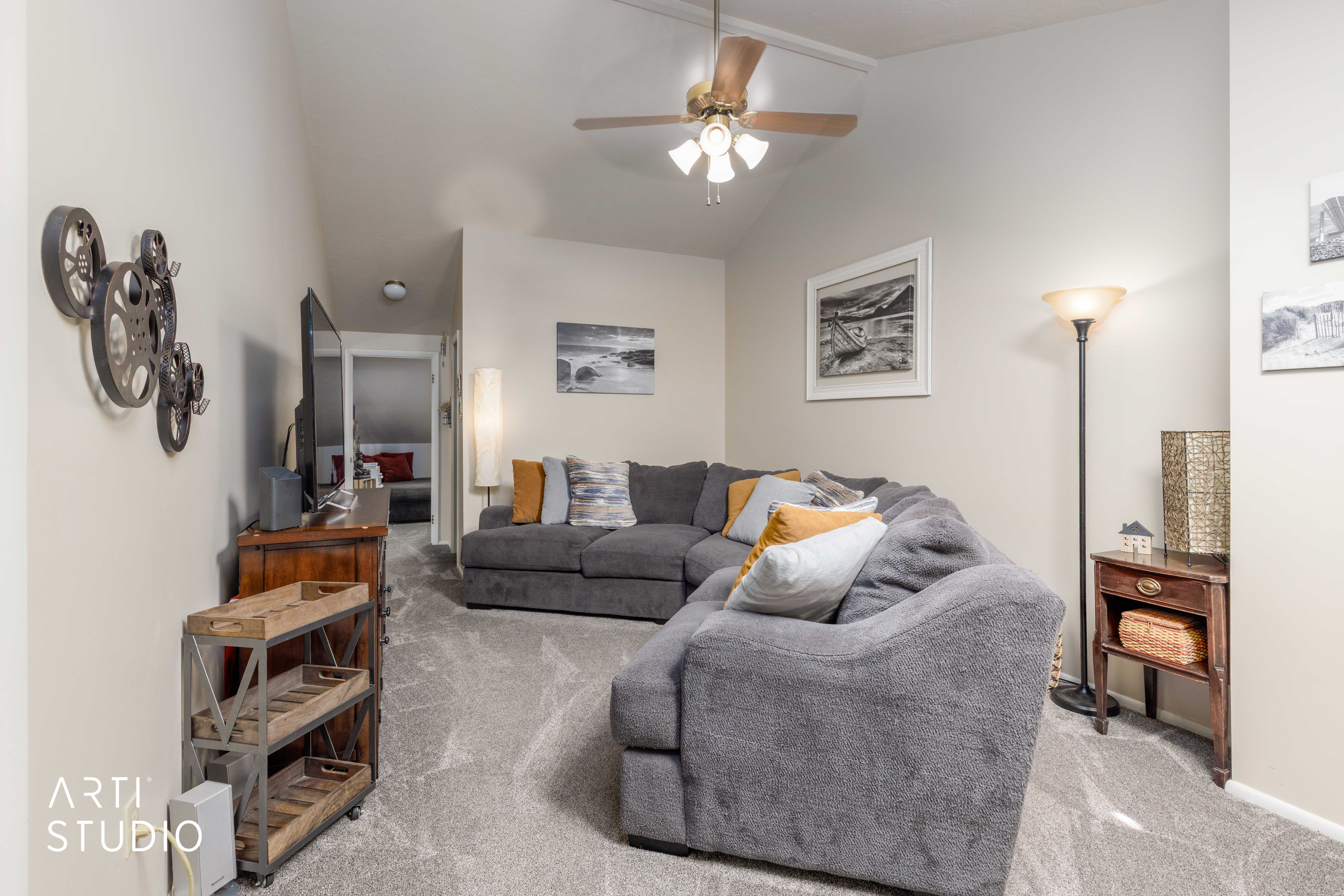 Vaulted ceilings with a ceiling fan, light-toned wall paint, and gray carpeting define this living area