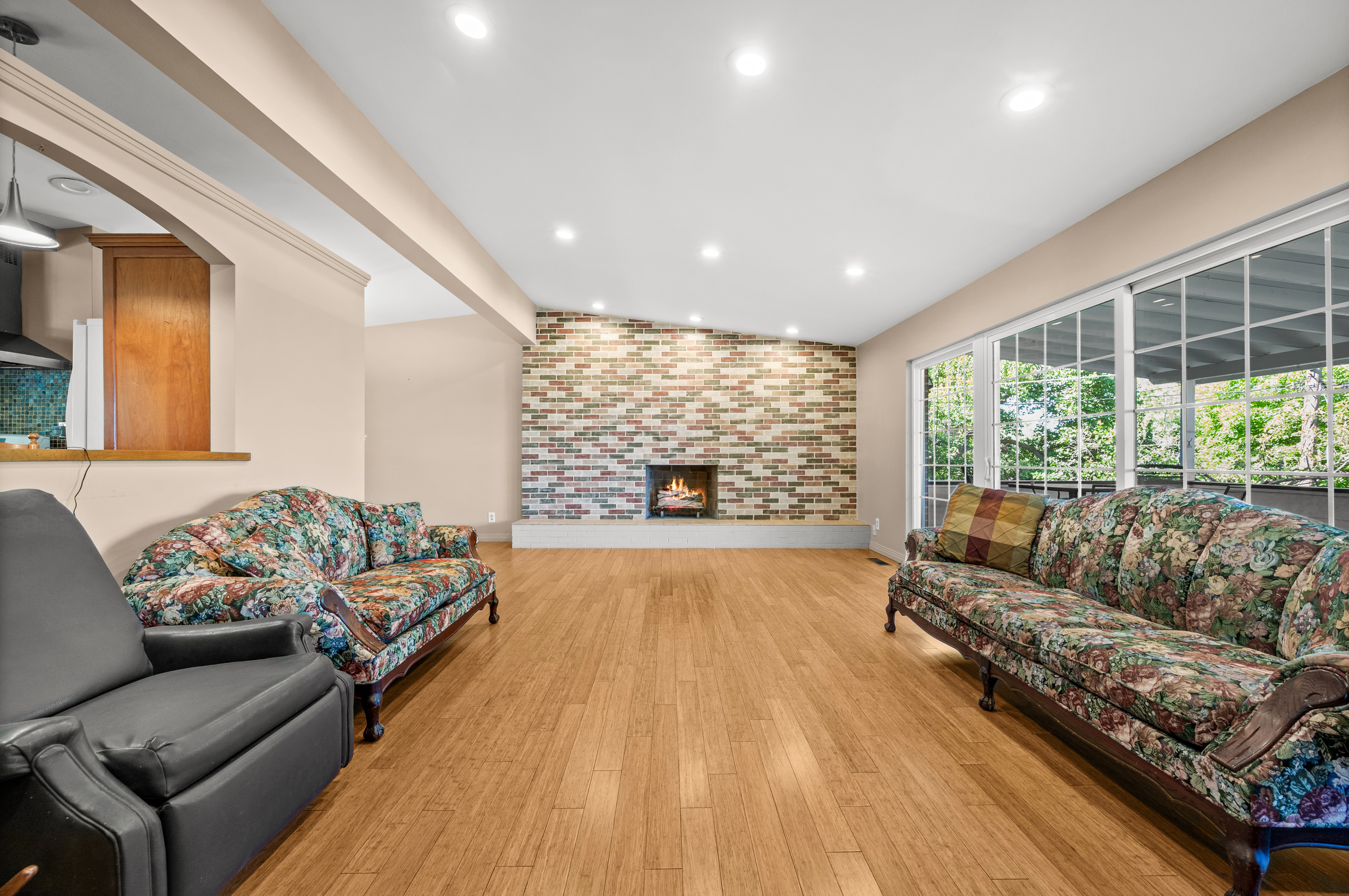 Spacious living area featuring wood-finish flooring, a contemporary fireplace with a brick surround, and large sliding glass doors
