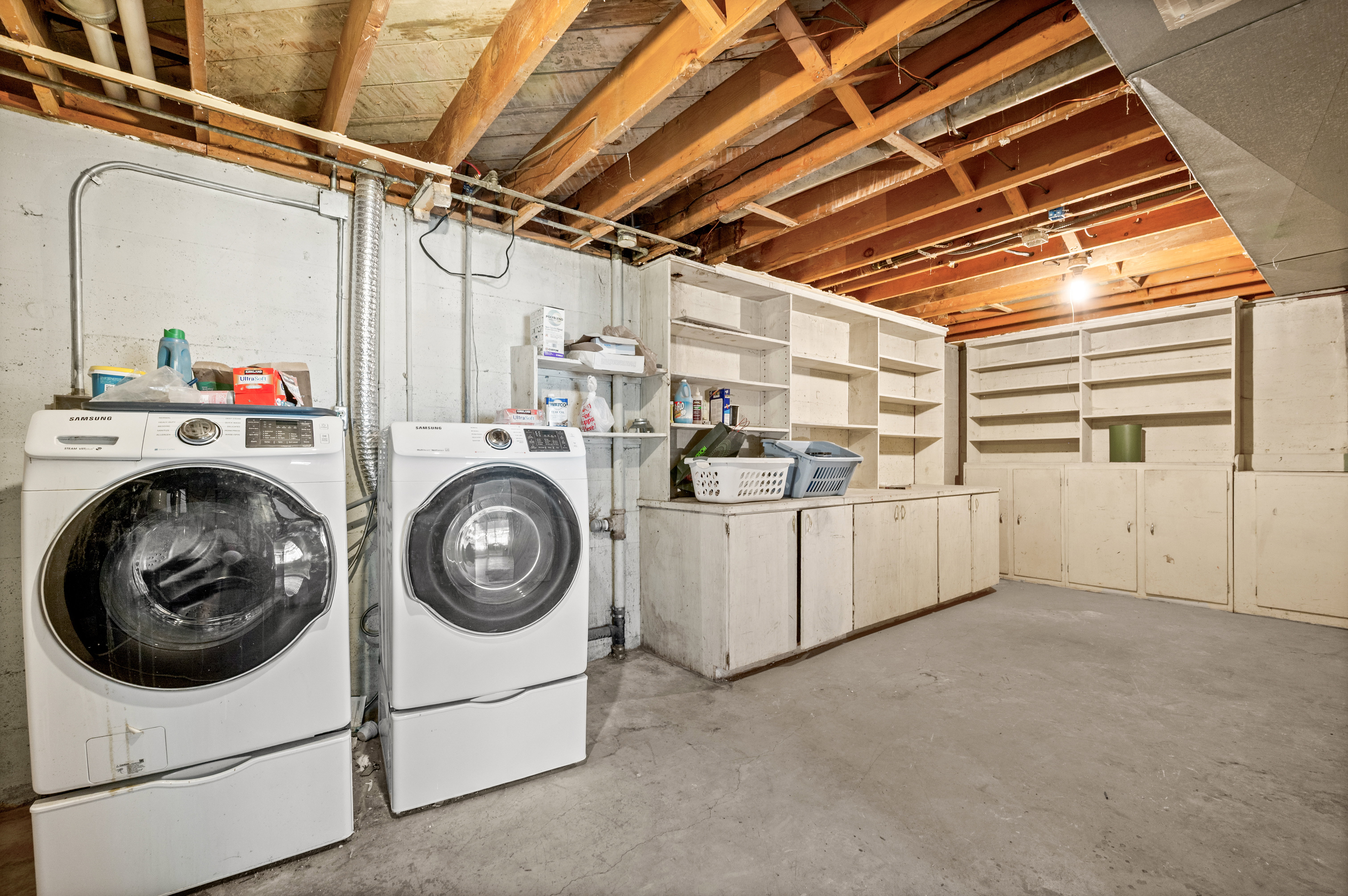 Unfinished basement space featuring exposed wood joists, concrete flooring, and built-in cabinetry with open shelving
