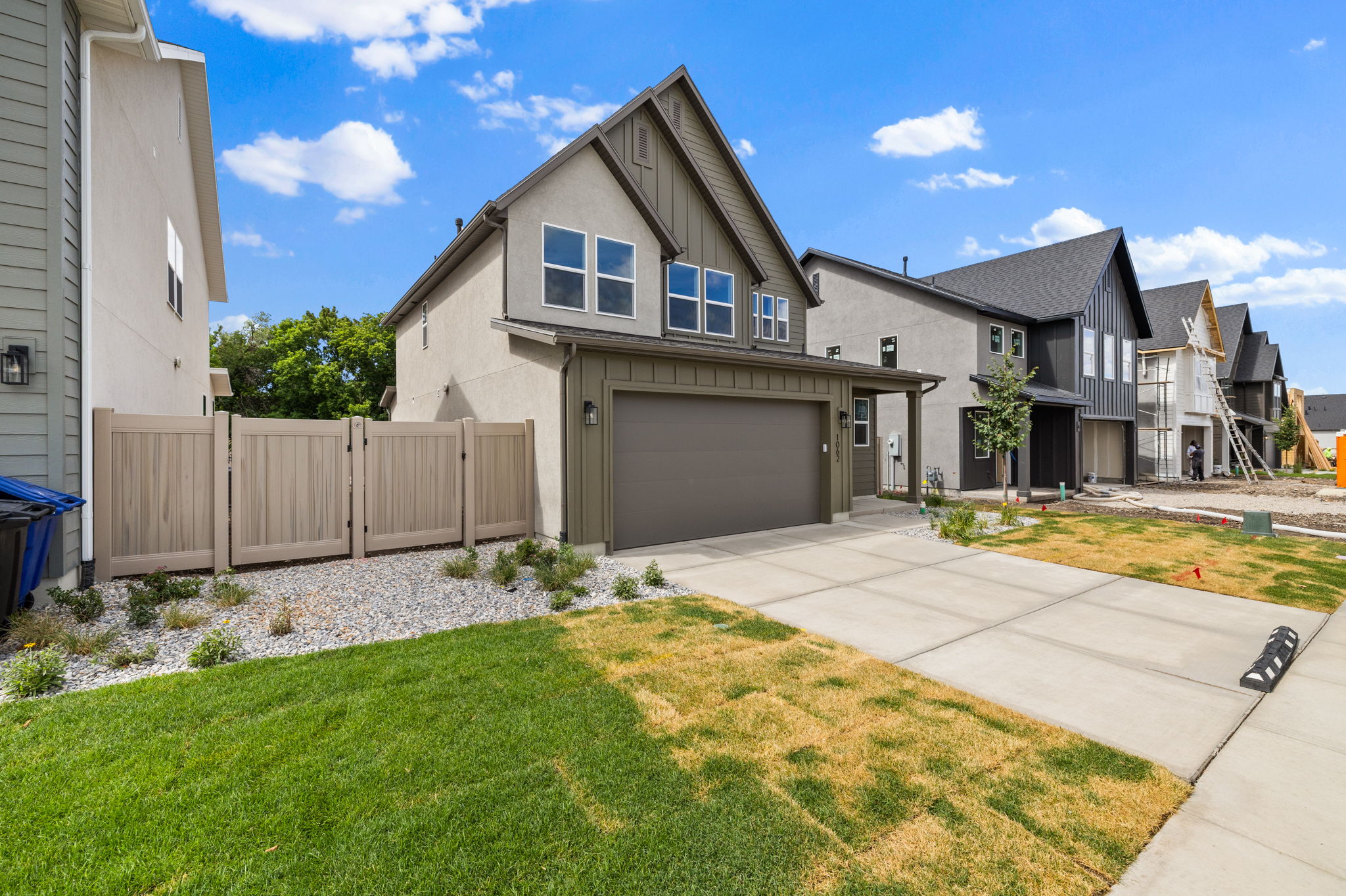 Contemporary two-story residence featuring a two-car garage, concrete driveway, and a fenced side yard with gravel landscaping