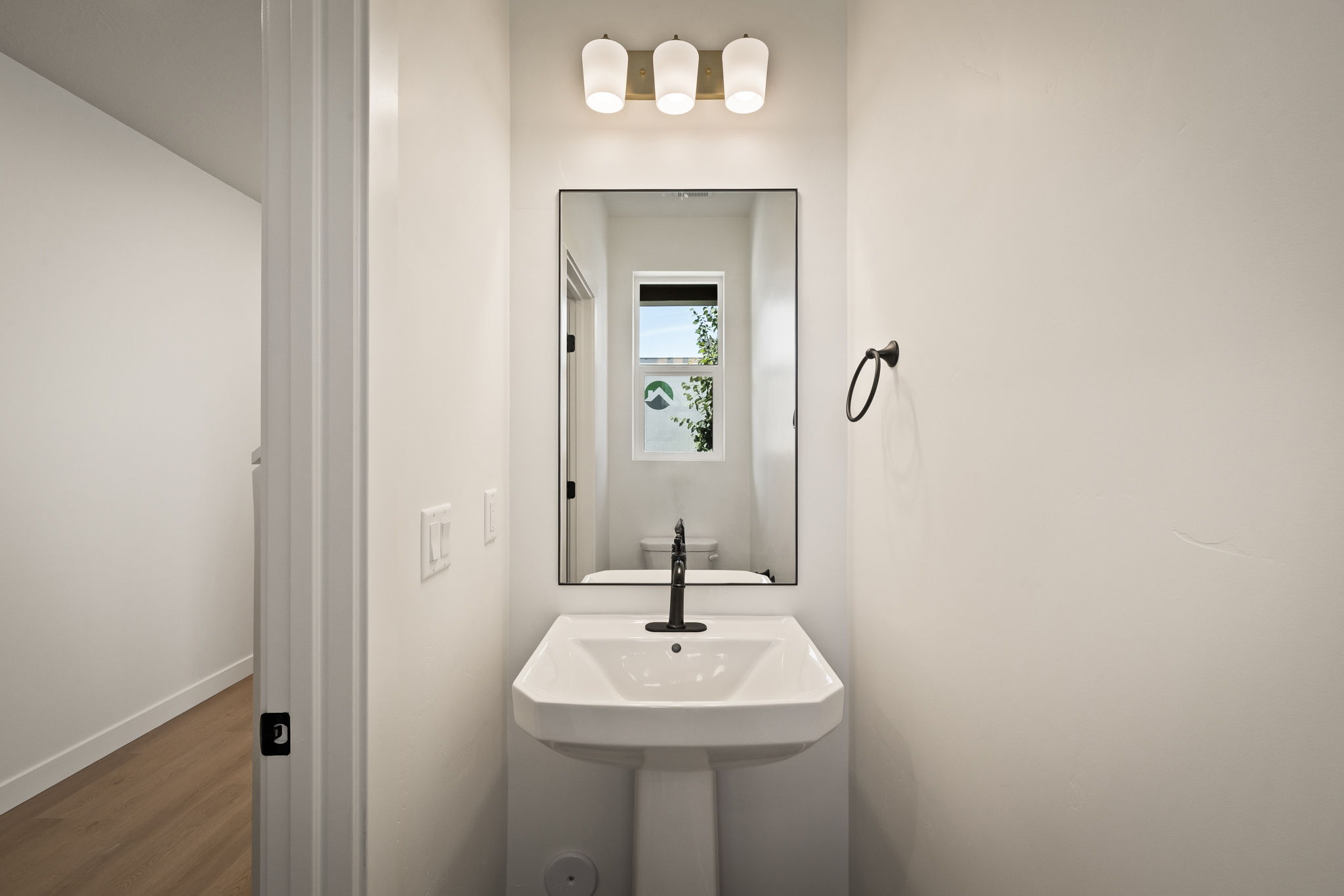 Pedestal sink with black wall-mounted faucet, rectangular mirror, and three-light vanity fixture
