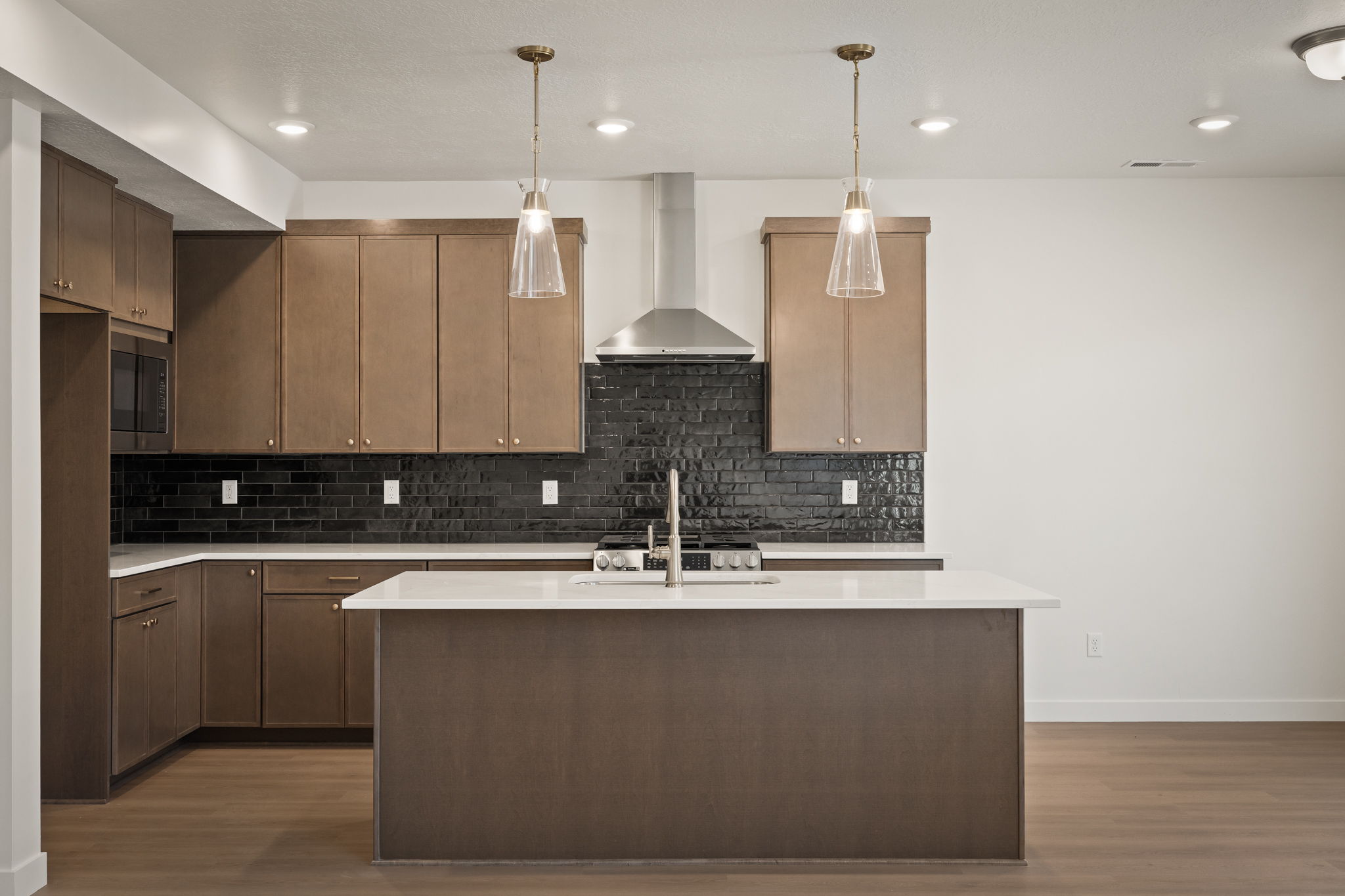 Modern kitchen featuring wood-finish cabinetry, a white countertop island, and a black subway tile backsplash