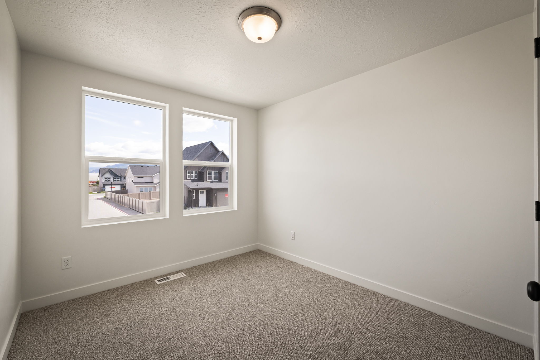 Neutral-toned interior room featuring two large windows, light grey wall paint, and a neutral carpeted floor