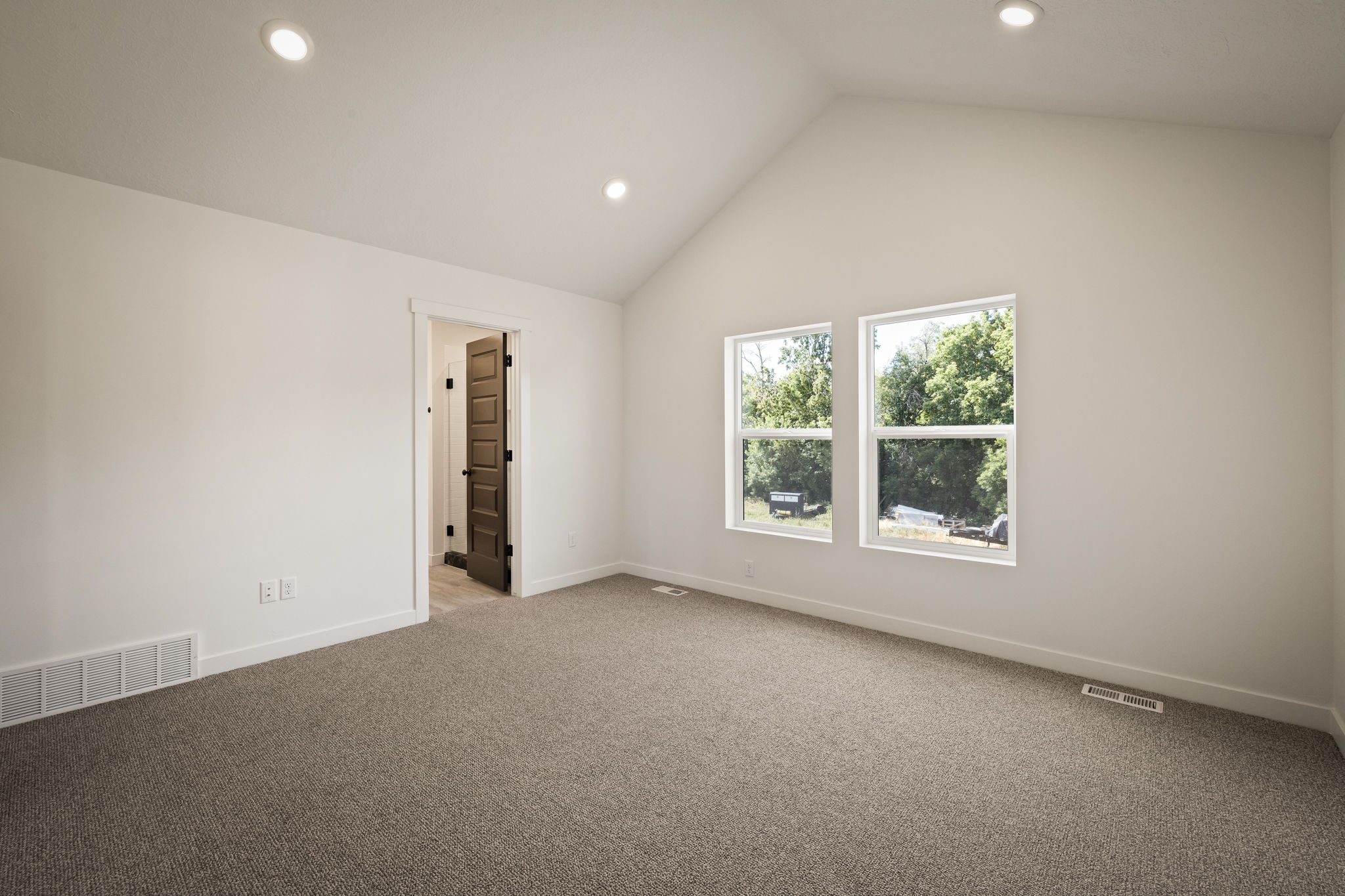 Spacious room featuring a vaulted ceiling with recessed lighting, two windows, wall-to-wall carpeting, and a dark paneled interior door