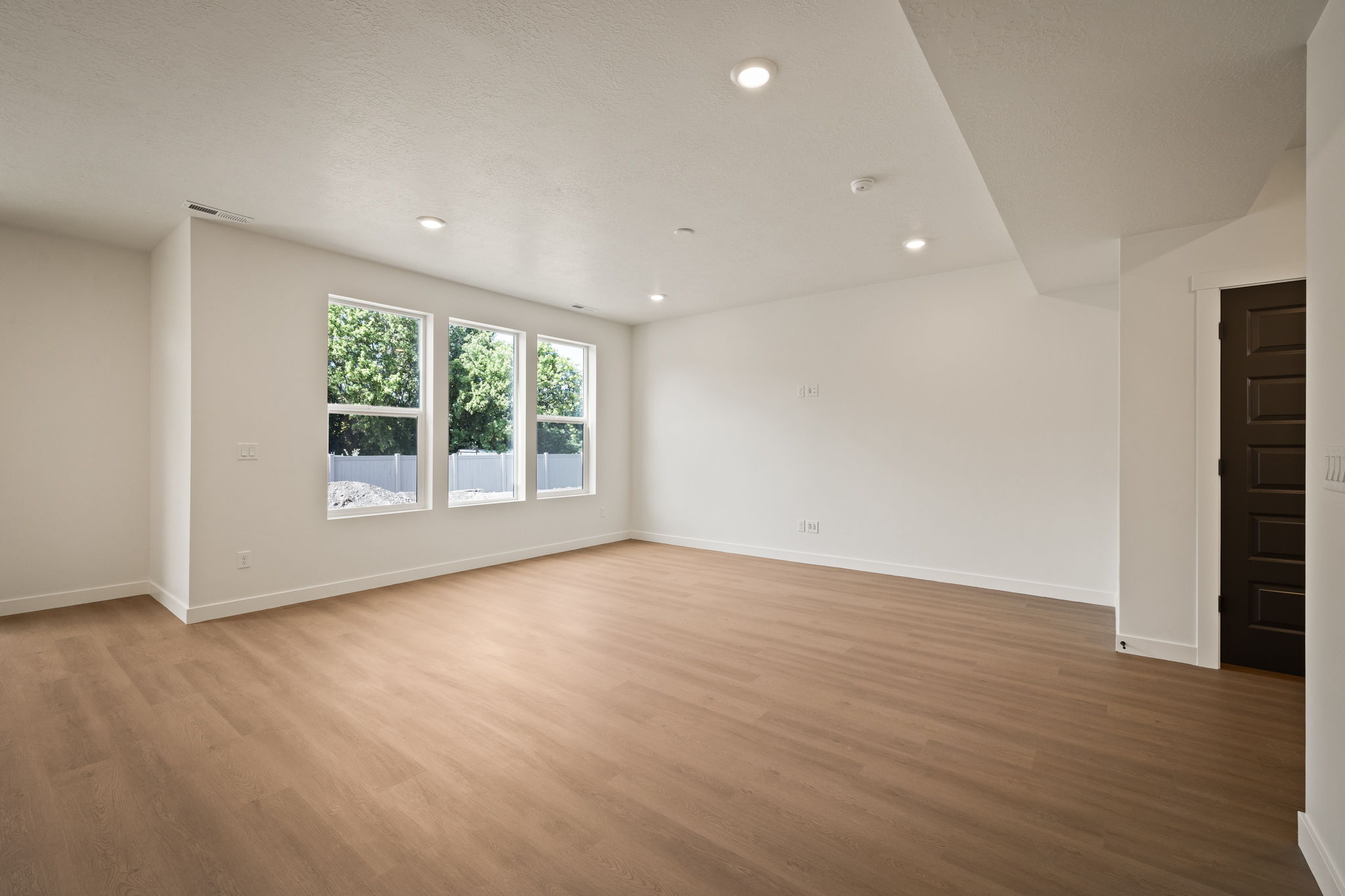 Spacious room featuring light wood-finish flooring, recessed lighting, and three tall windows