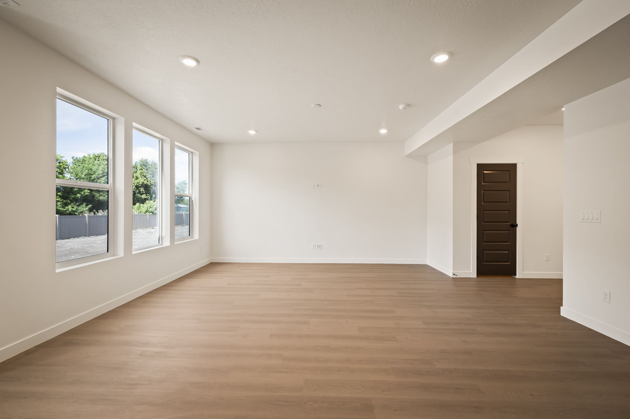 Spacious interior with wood-finish flooring, recessed lighting, and a dark paneled door