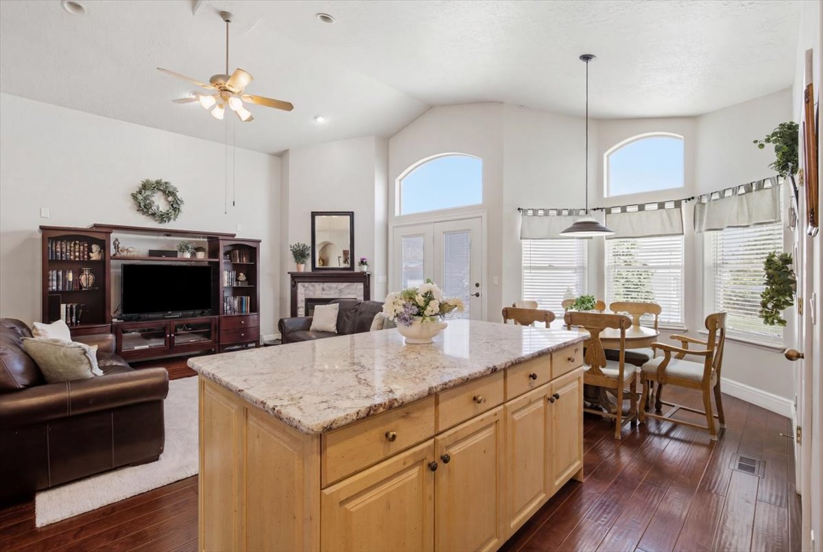 Kitchen island with granite countertop, wood-finish flooring, vaulted ceilings, recessed lighting, and arched windows