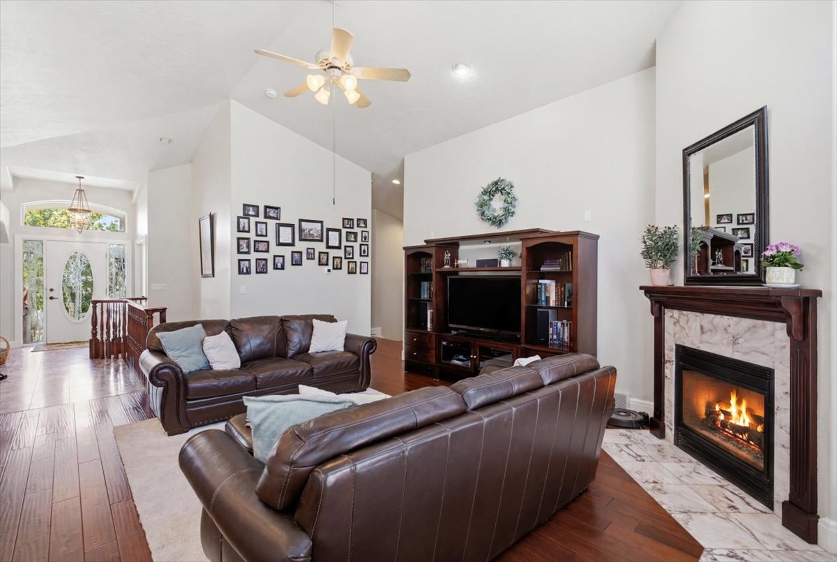 Living area featuring a fireplace with a stone surround and wood mantel, vaulted ceilings, and wood-finish flooring