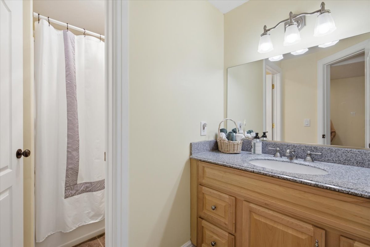 Bathroom vanity featuring a light wood-finish cabinet with drawer and door storage, a speckled countertop, and an undermount sink with a chrome faucet