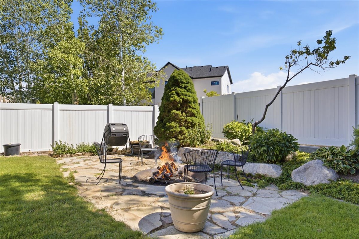 Backyard featuring a stone paver patio with fire pit, manicured lawn, and mature landscaping