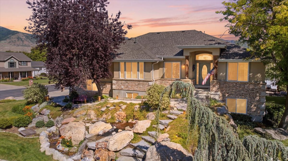 Stucco and stone facade home featuring a prominent entryway, multi-level landscaping with a rock garden, established trees, and a visible mountain backdrop