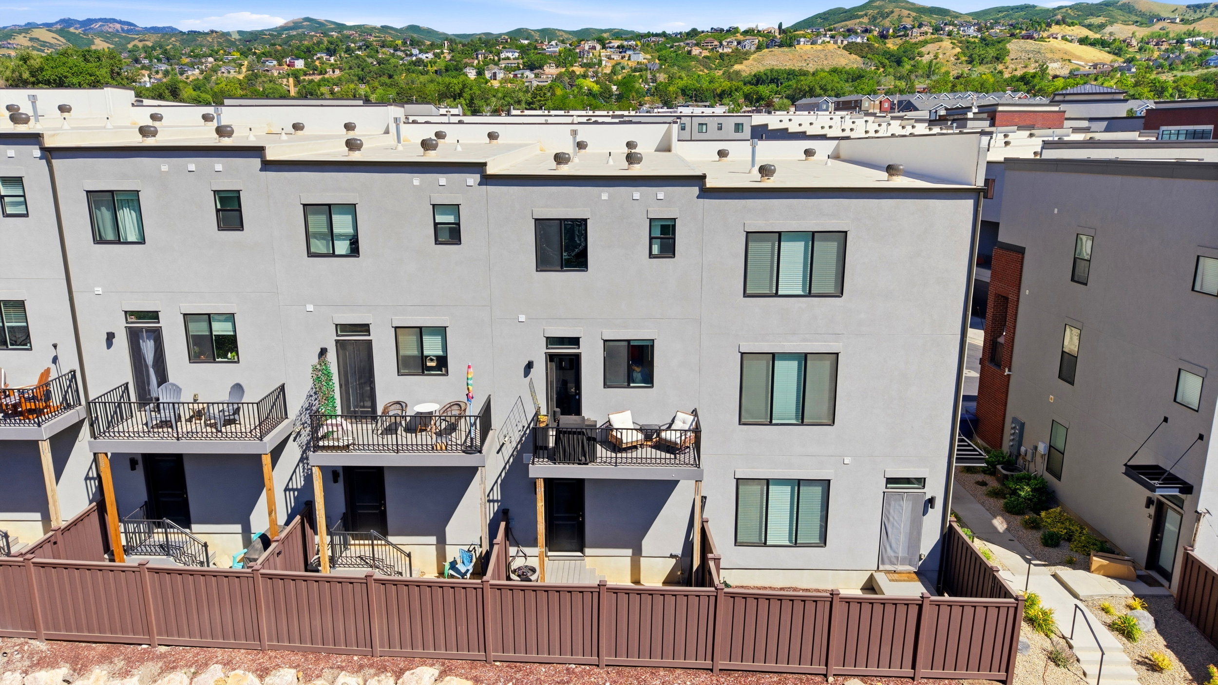 Contemporary multi-story exterior featuring a private balcony with black metal railings, a fenced yard, and multiple large windows