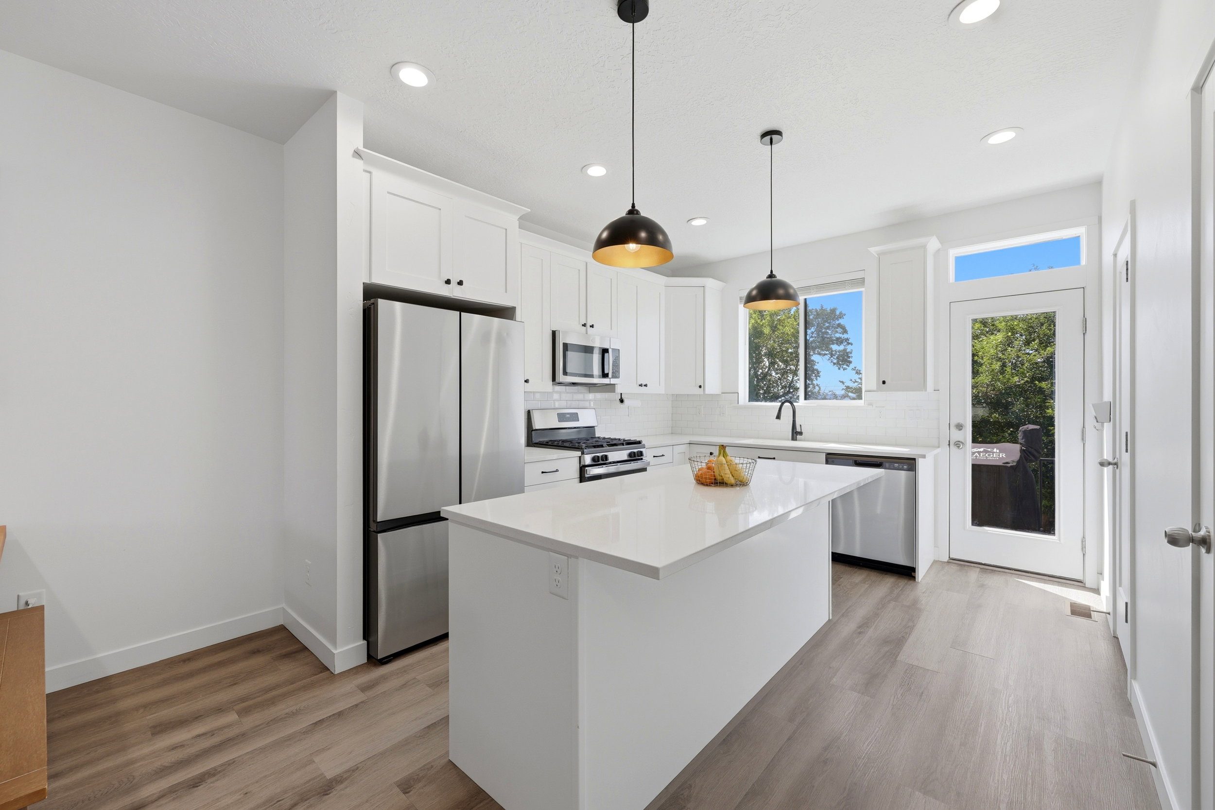 Modern kitchen featuring a central island with a white countertop, white cabinetry, stainless steel appliances, and wood-finish flooring