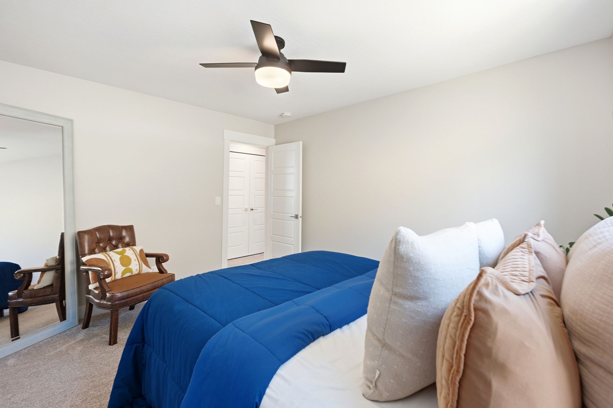 Light-filled bedroom featuring neutral wall tones, textured carpeting, a contemporary ceiling fan, and double bi-fold closet doors
