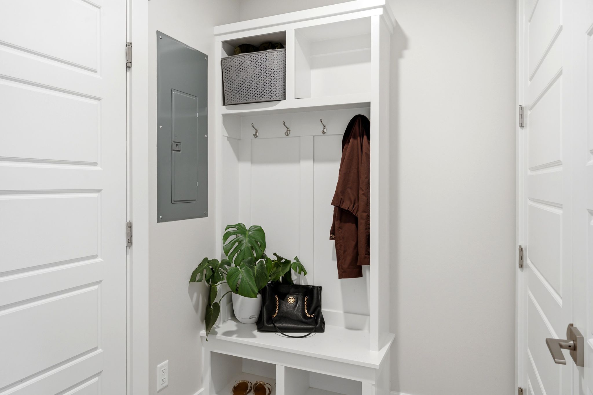 Built-in white mudroom bench and shelving unit featuring coat hooks and upper storage cubbies
