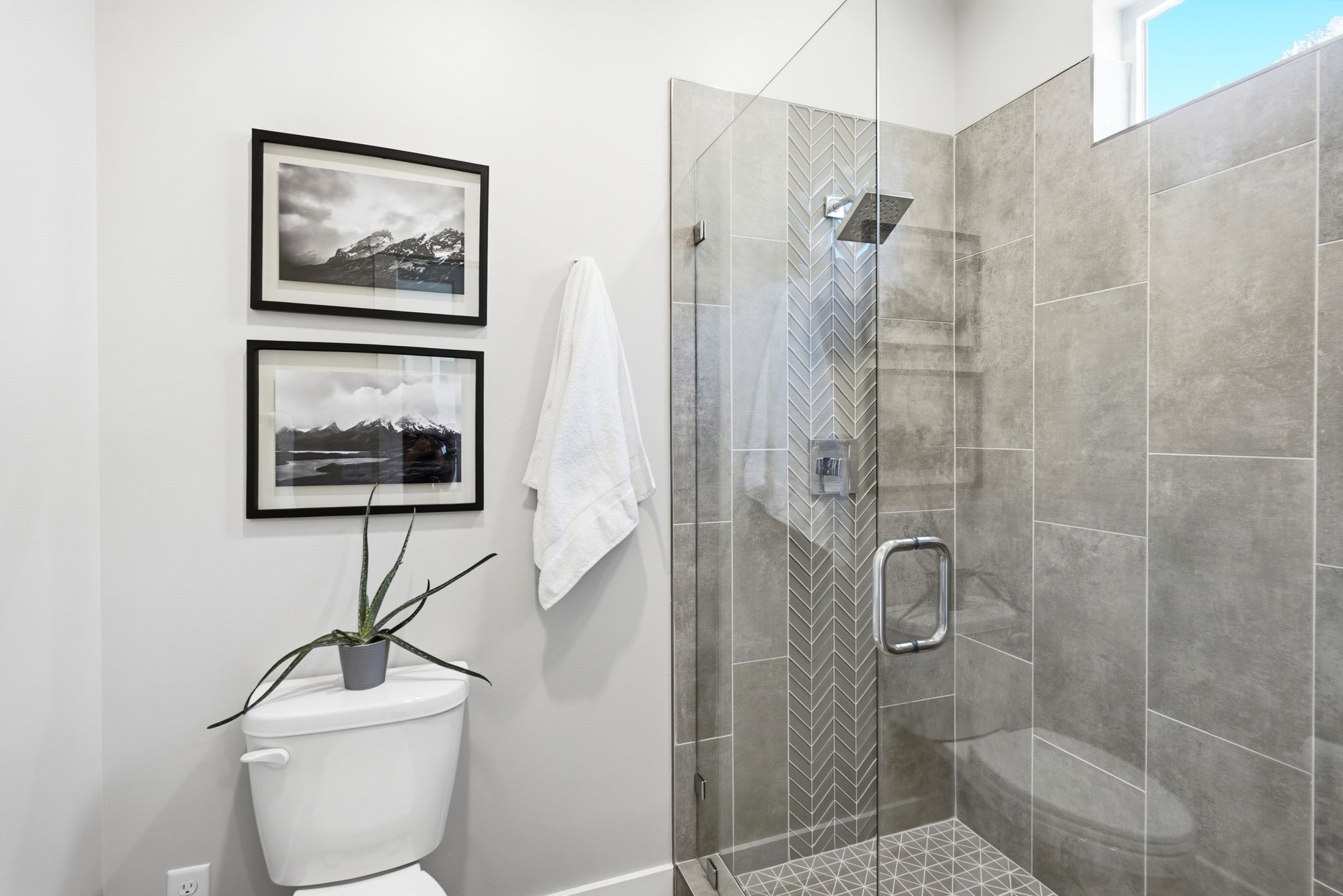 Glass-enclosed shower featuring large format wall tiling, a herringbone-patterned accent strip, and a rainfall showerhead
