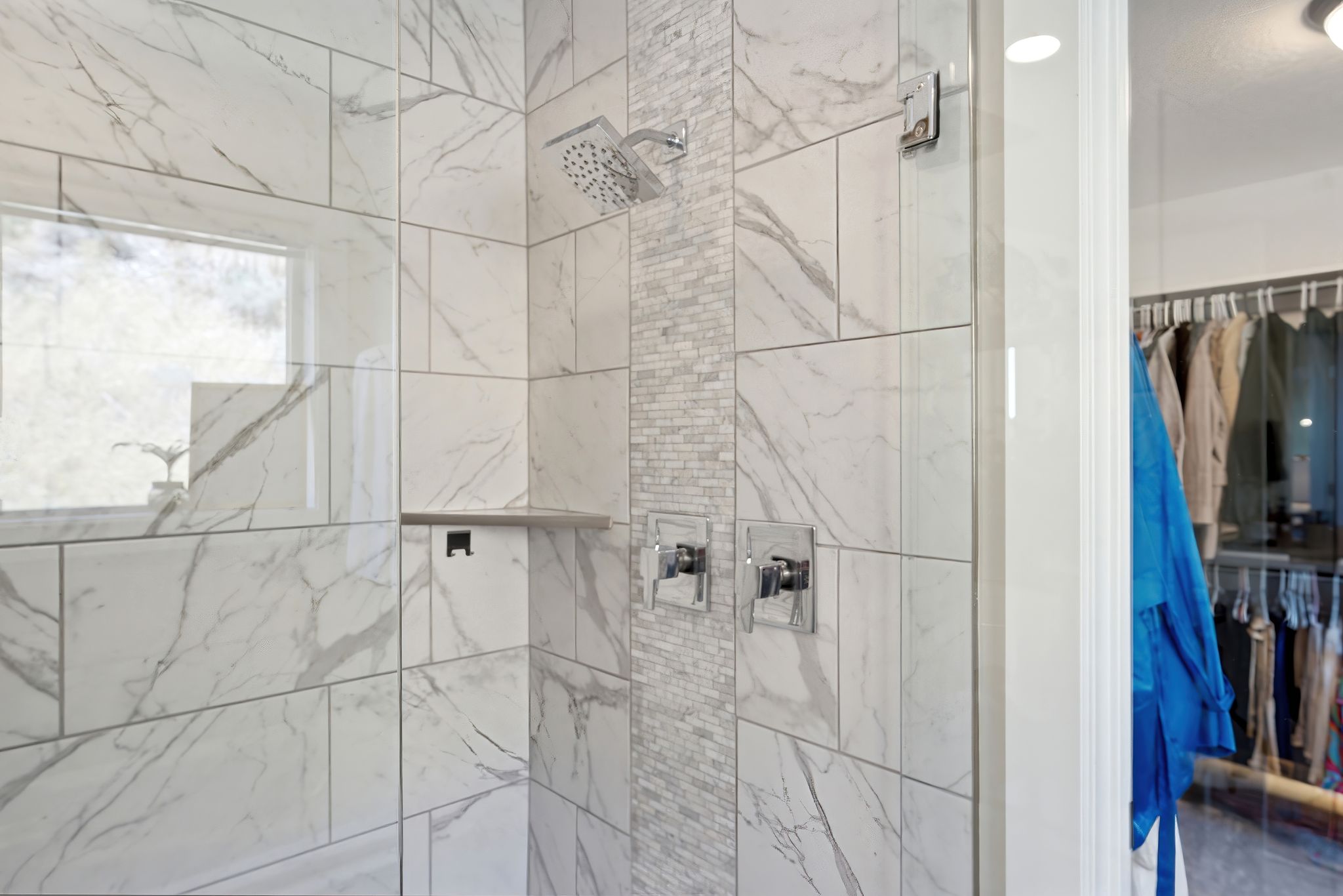 Walk-in shower with marble-look tile, mosaic tile accent, chrome fixtures, and a built-in shower niche