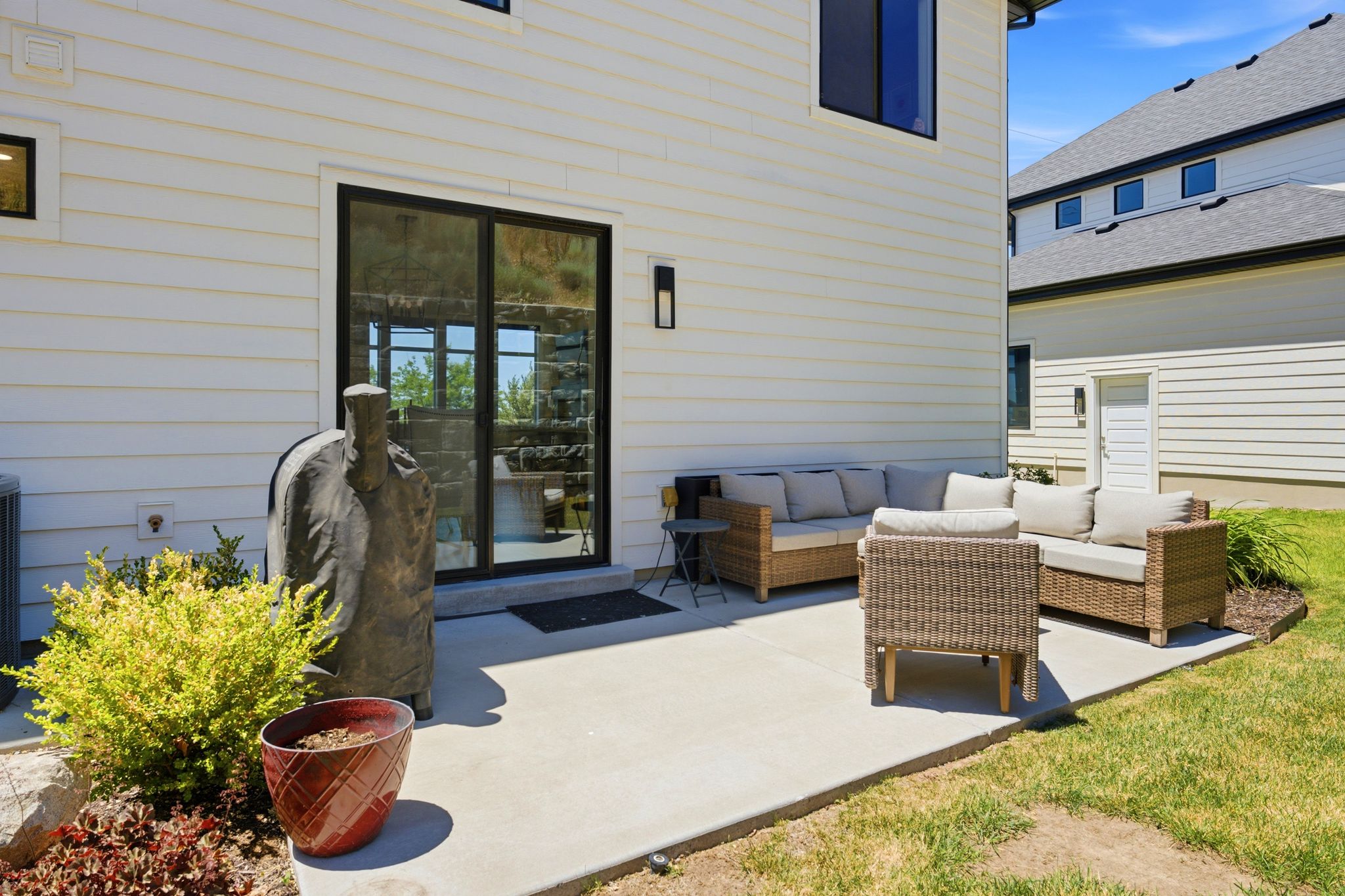 Spacious concrete patio with sliding glass door access, white horizontal siding, and black window trim