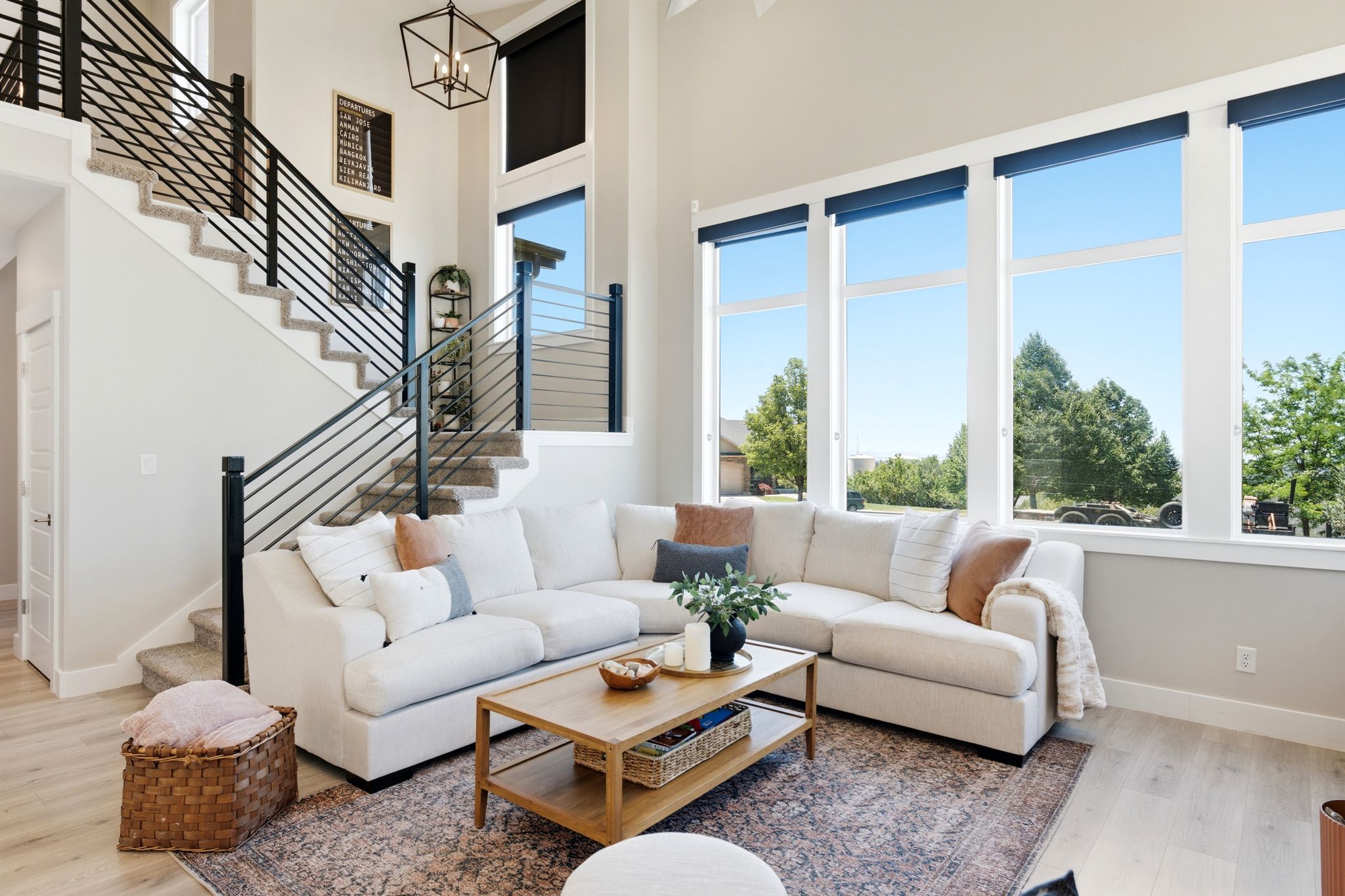 Two-story great room featuring a tall wall of windows, high ceilings, light wood-finish flooring, and a modern horizontal bar stair railing