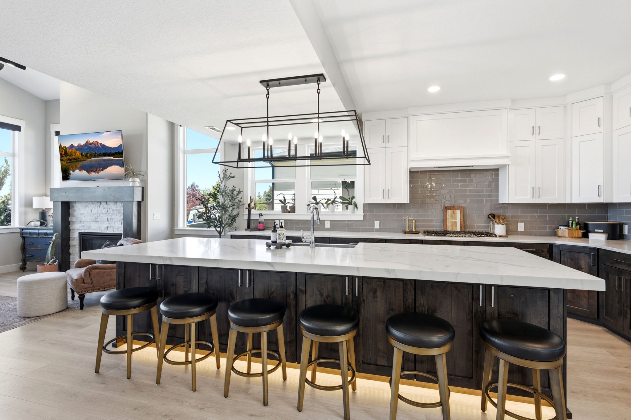 Open-concept kitchen featuring an expansive center island with seating for four, white perimeter cabinetry, a subway tile backsplash, and light wood-finish flooring